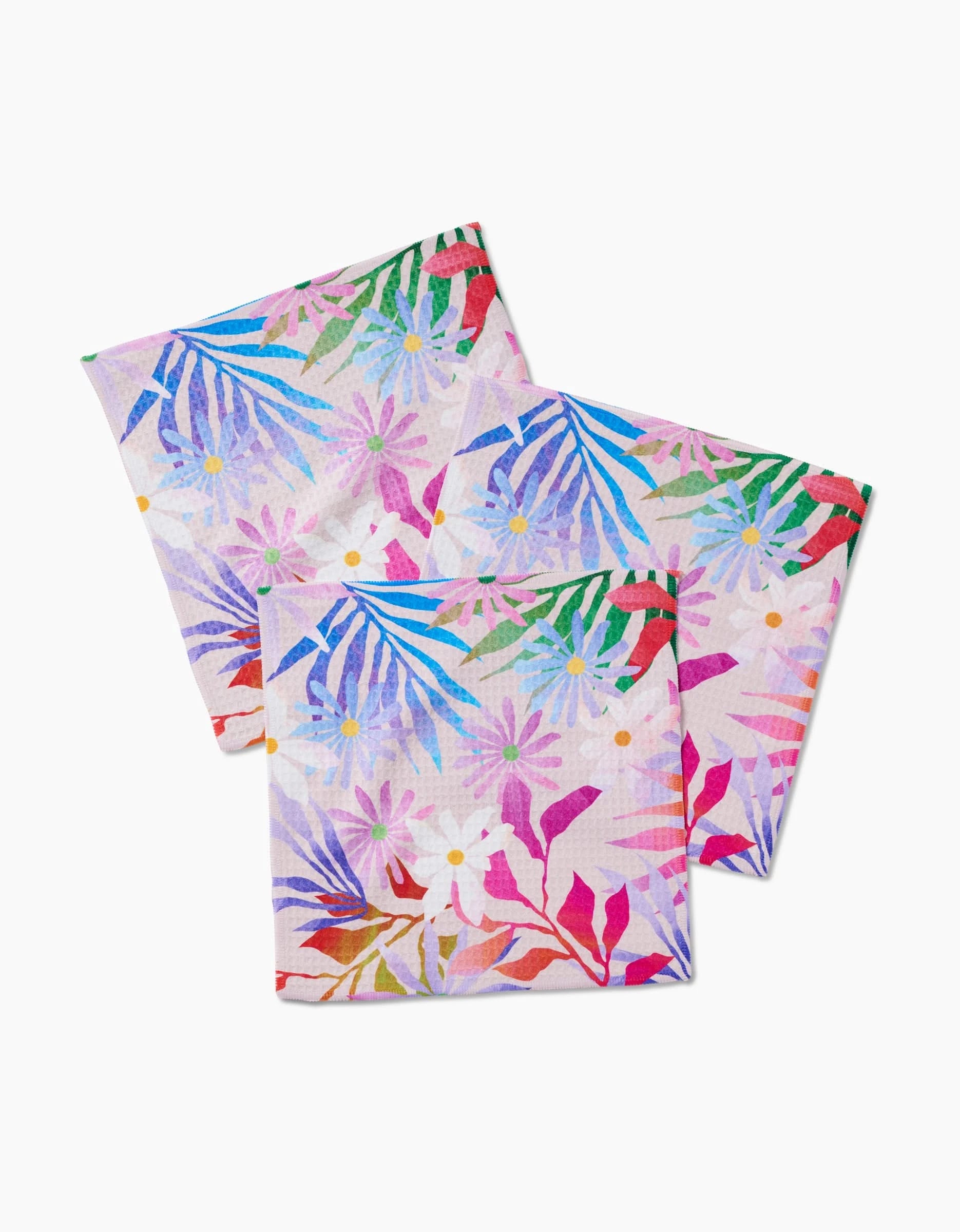 Three Bold Blossoms napkins by GEOMETRY, featuring a vibrant floral and leaf pattern in pink, purple, blue, green, and red on white. Made with Geoweave technology for an ultra-absorbent Luxe Washcloth feel.