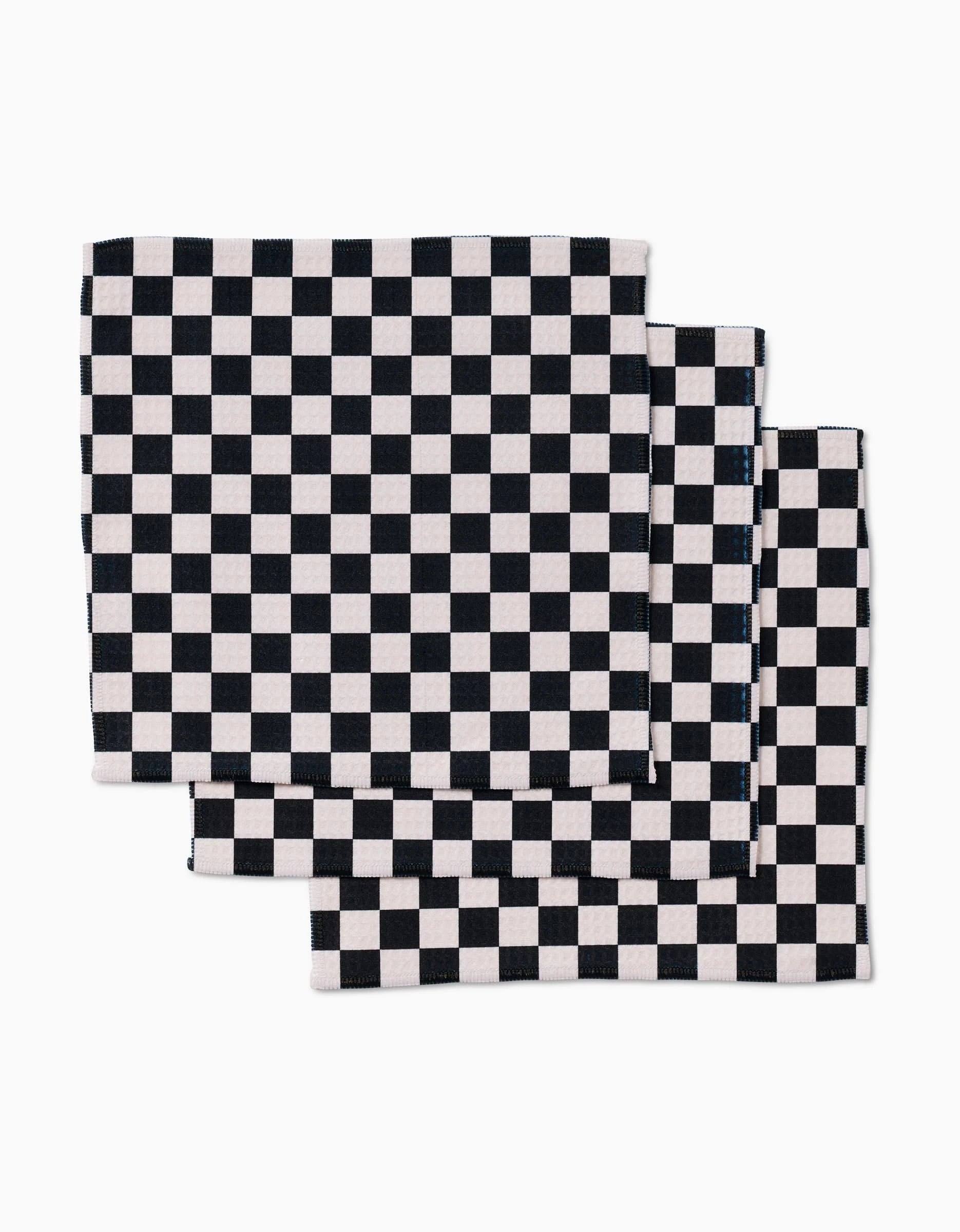 Four ultra-absorbent GEOMETRY Checkered cloth napkins, featuring a black and white checkerboard design, are neatly stacked with slight overlap on a white background.