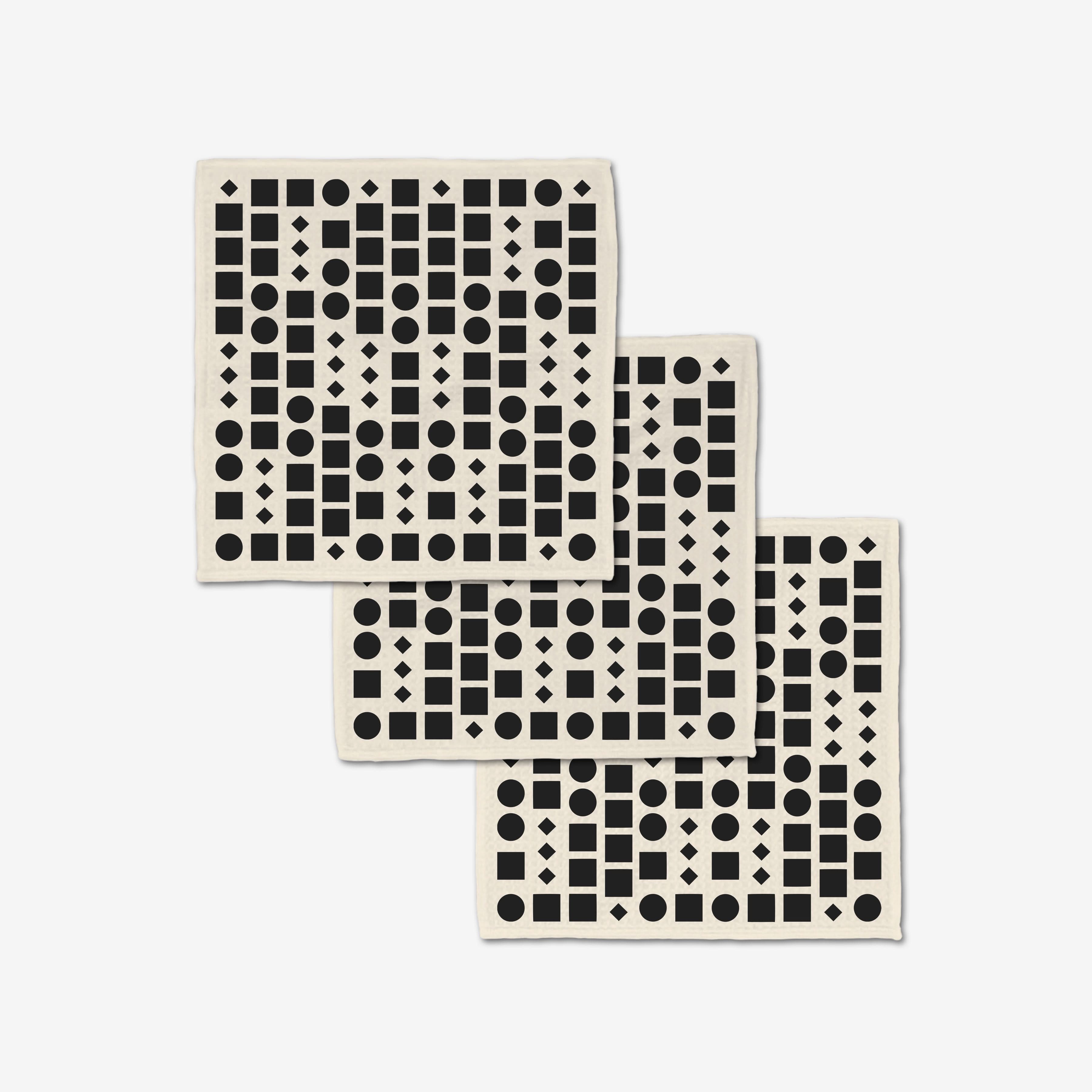 Three overlapping Coded washcloths by GEOMETRY showcase black circles, squares, triangles, and diamonds on white. Crafted from post-consumer recycled materials, these ultra-absorbent washcloths combine style and sustainability.