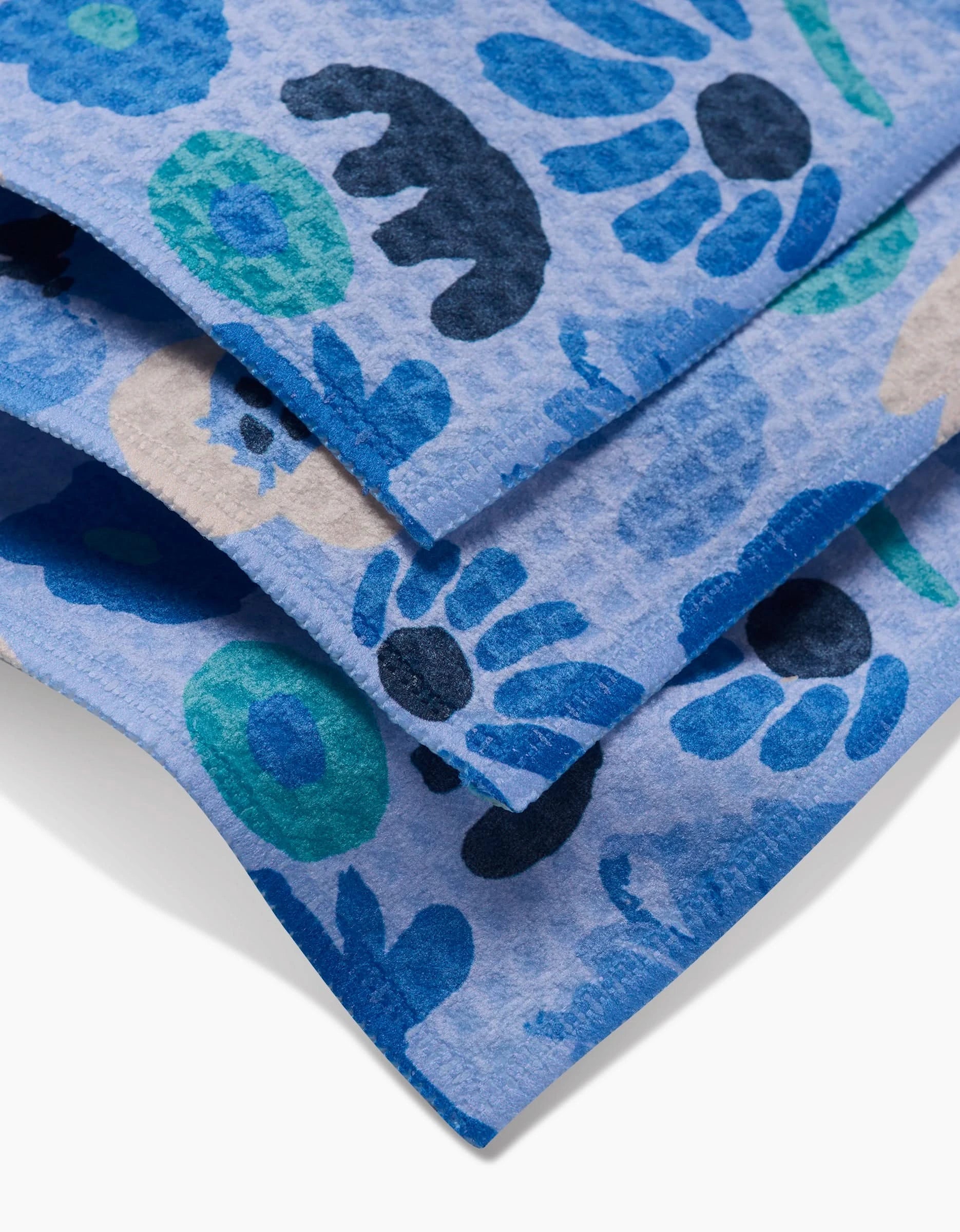 Close-up of folded blue Sareka Unique Cool Blooms washcloths featuring playful animal and floral prints in blue tones on a light background, crafted with ultra-absorbent Geoweave technology.