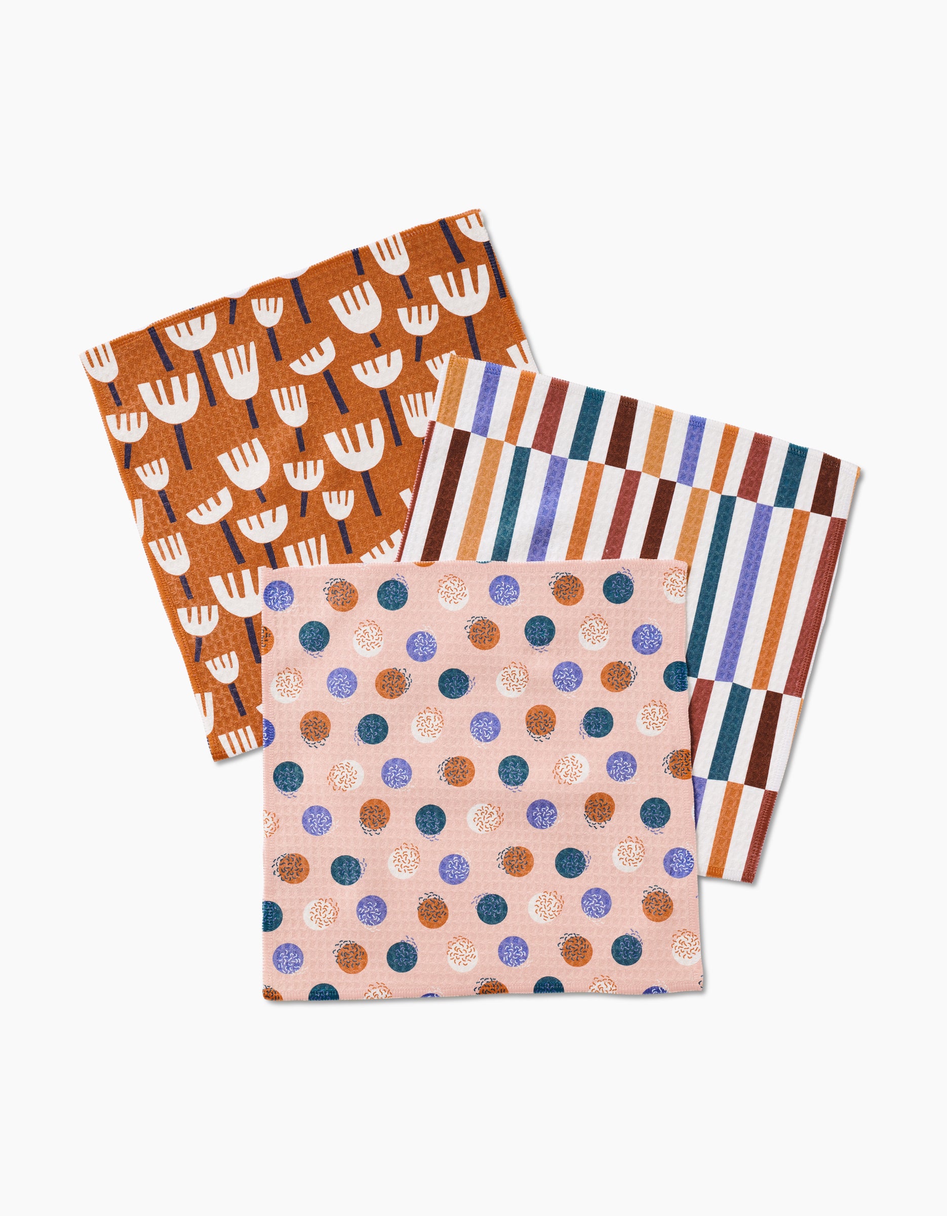 Three folded cloth napkins from Claire Iglesias’s Cutout Shapes collection—featuring unique patterns and crafted with ultra-absorbent Geoweave technology—for a luxurious washcloth feel.