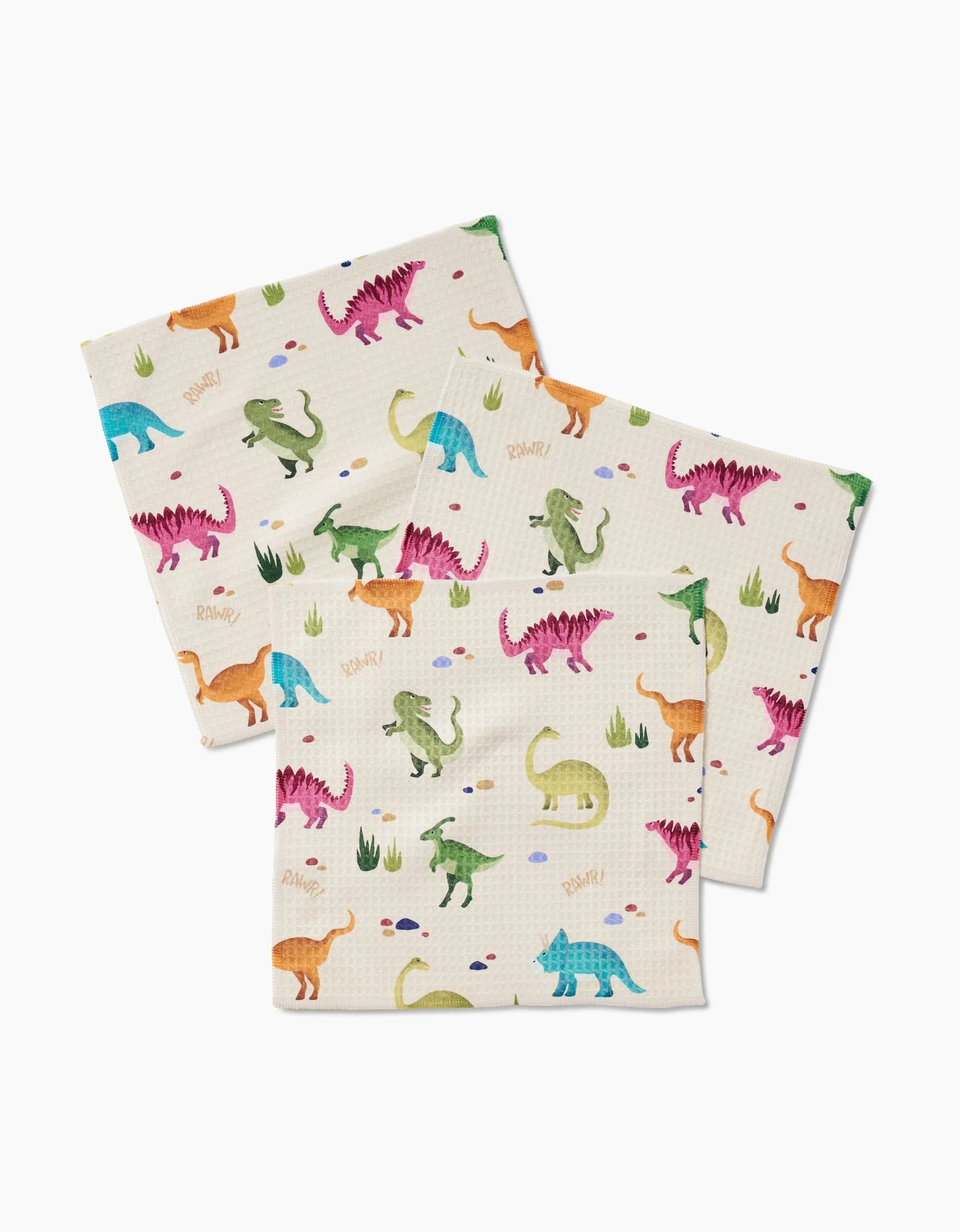 Three ultra-absorbent GEOMETRY Luxe Washcloths in the Dancing Dinos pattern, featuring colorful dinosaurs, green grass, and eggs on a white background.