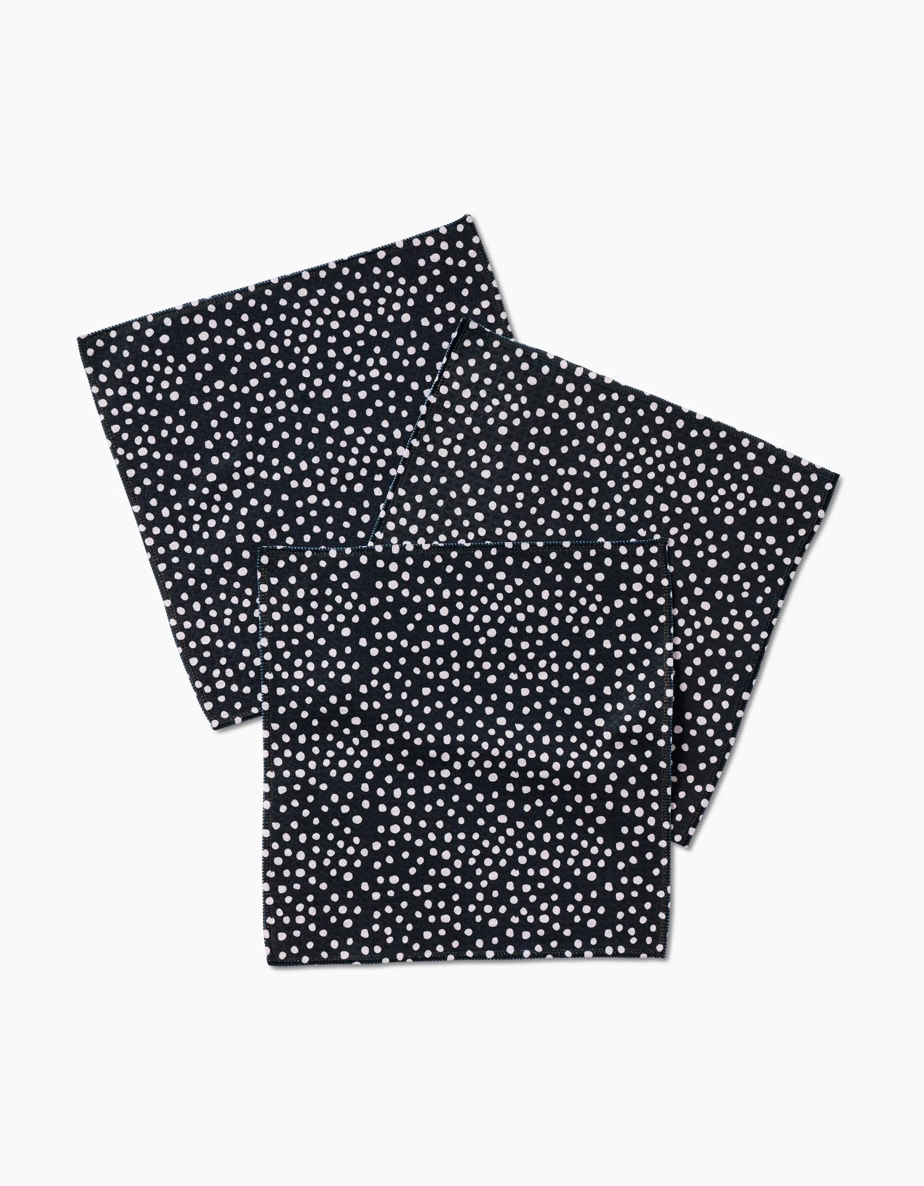 Two folded GEOMETRY Dotty Black napkins, featuring an even pattern of small white polka dots and crafted with ultra-absorbent Geoweave technology, are displayed on a white background.