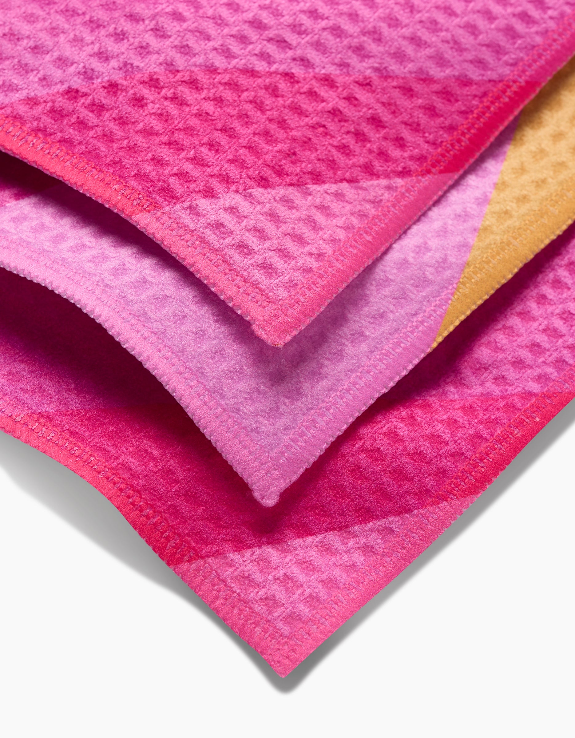 The GEOMETRY Electric Pink washcloth set features three stacked waffle-patterned fabrics in pink, purple, and orange shades, each with neatly finished edges for a stylish and ultra-soft touch.