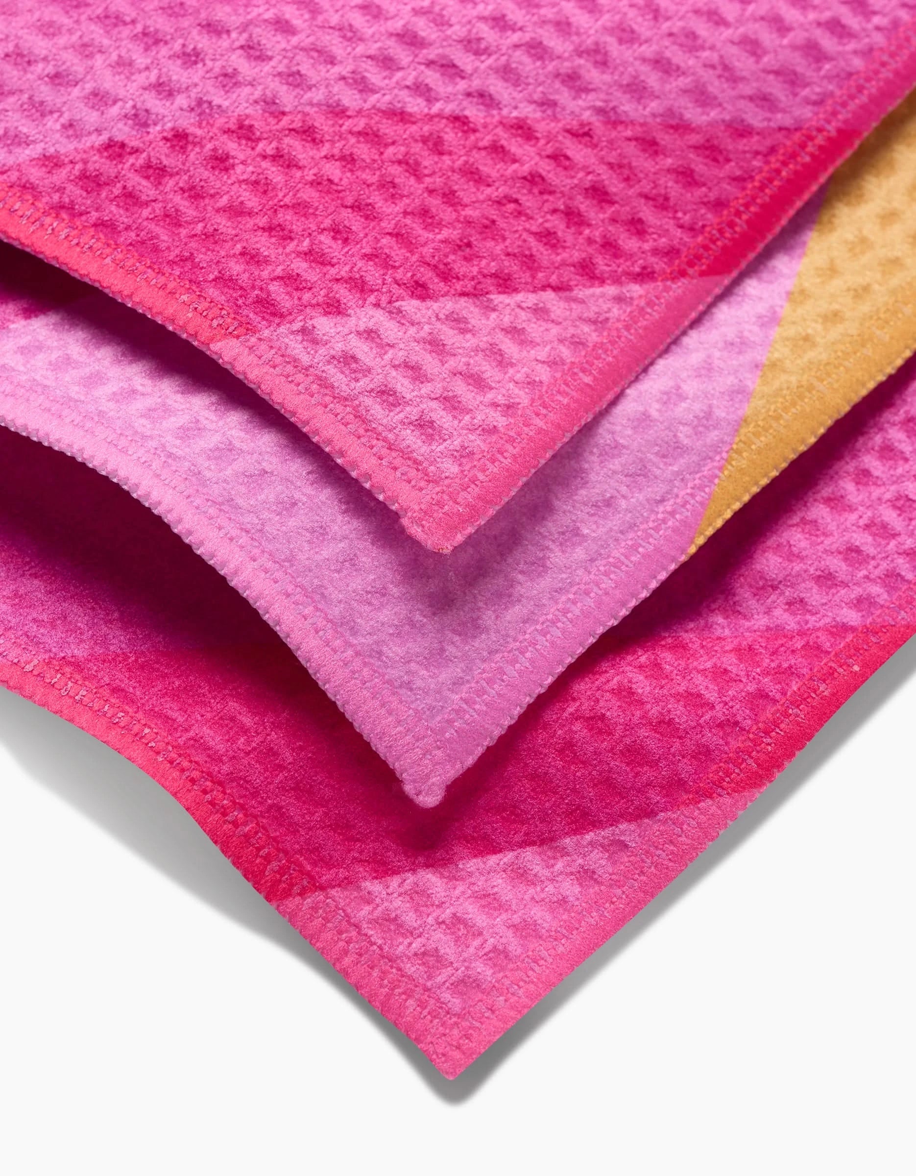 The GEOMETRY Electric Pink washcloth set features three stacked waffle-patterned fabrics in pink, purple, and orange shades, each with neatly finished edges for a stylish and ultra-soft touch.