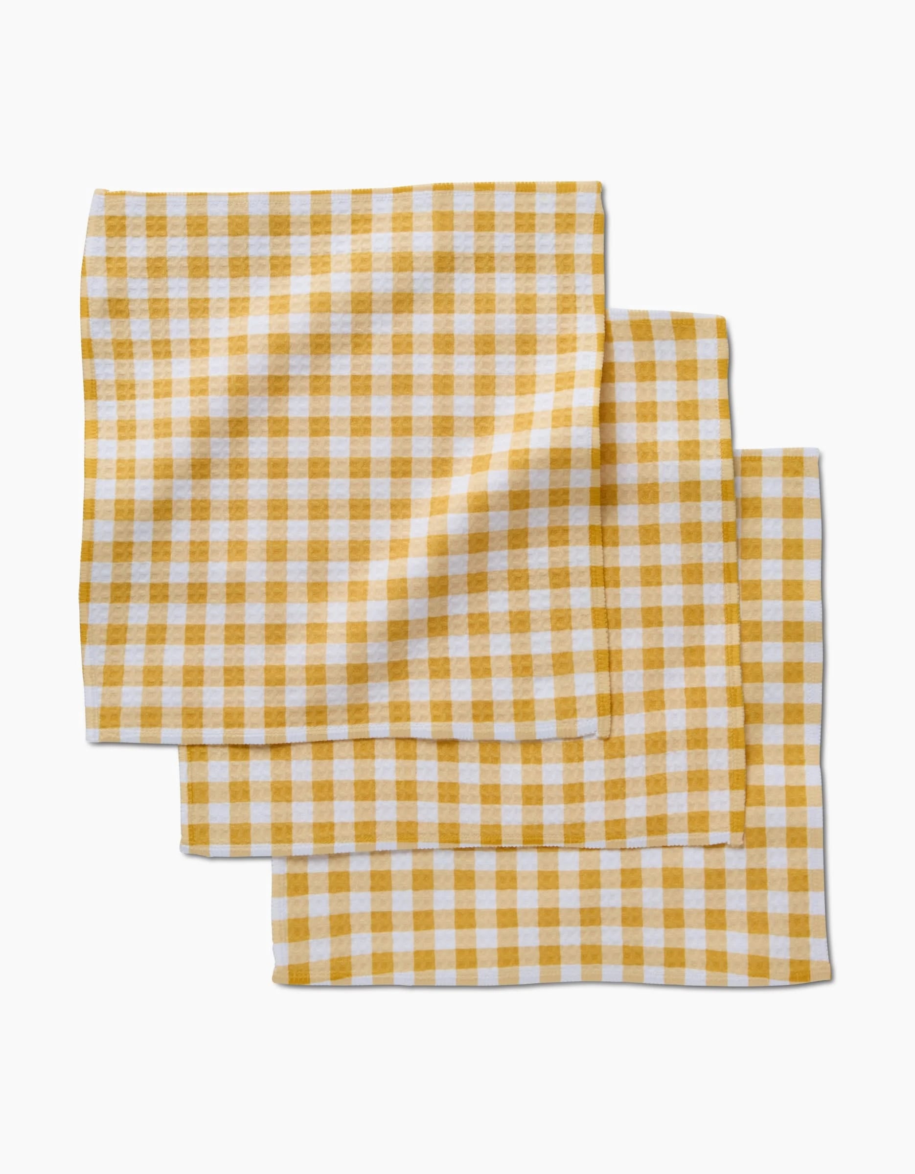 Three folded Golden Plaid napkins by Danelys Sidron, featuring yellow and white checks with Geoweave technology, are stacked on a white background.