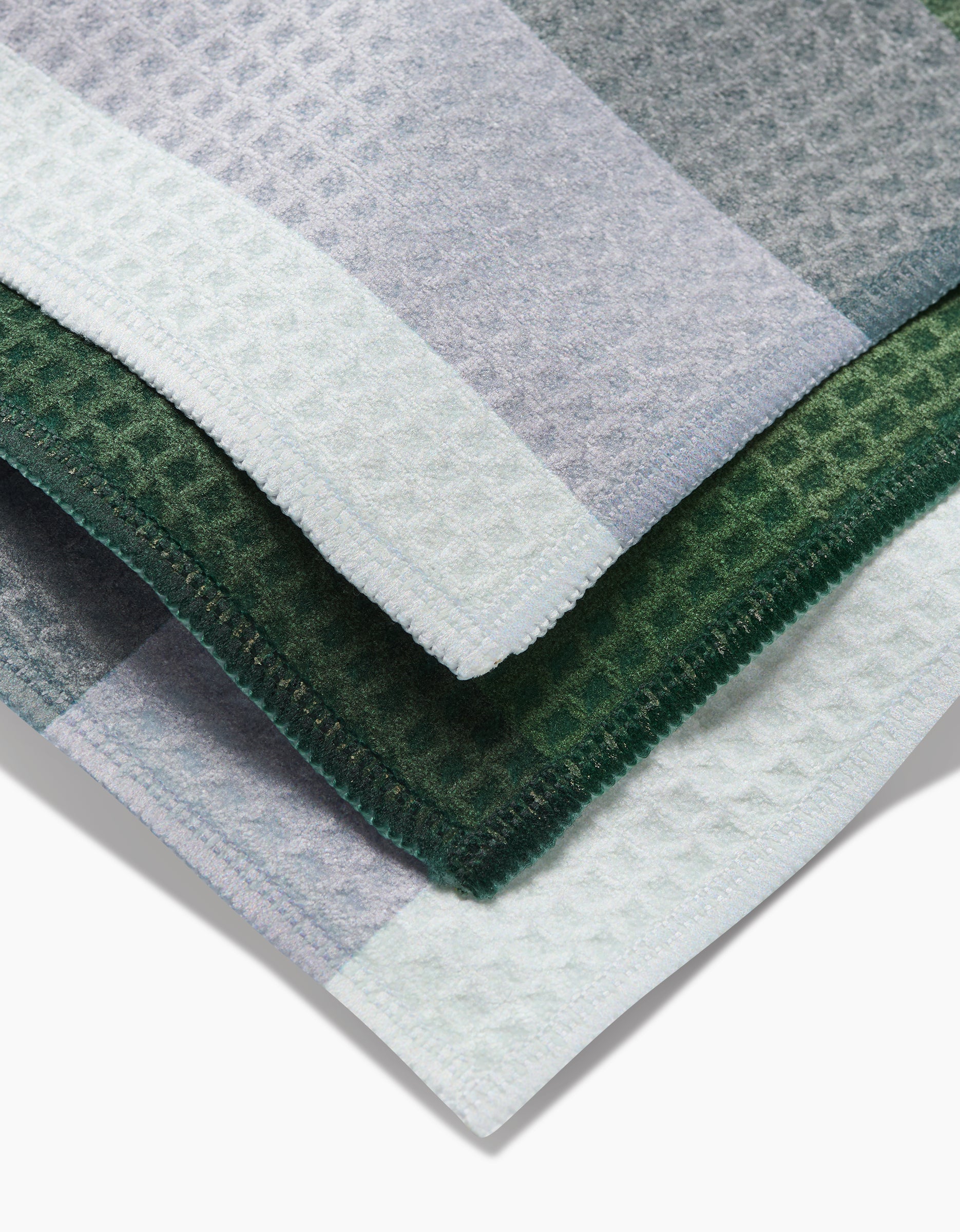 A close-up of overlapping GEOMETRY Grassy Levels washcloths in green, gray, and white highlights their ultra-absorbent Geoweave fabric and neatly stitched edges.