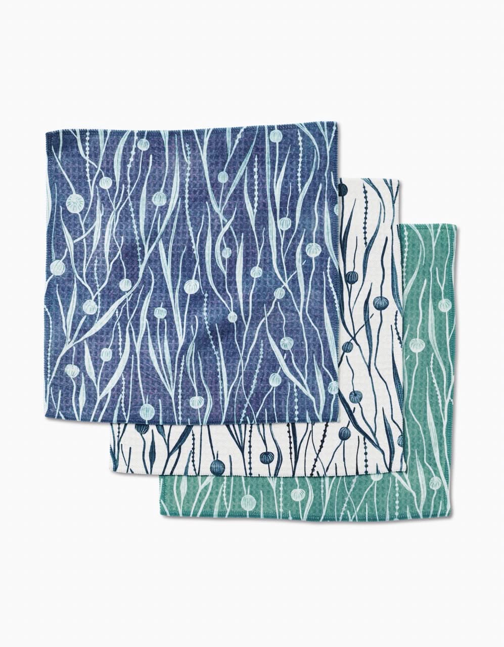 Three Kelp washcloths by Katie OShea—blue, white, and green with botanical patterns—are stacked atop one another on a white background. Crafted with ultra-absorbent Geoweave technology.