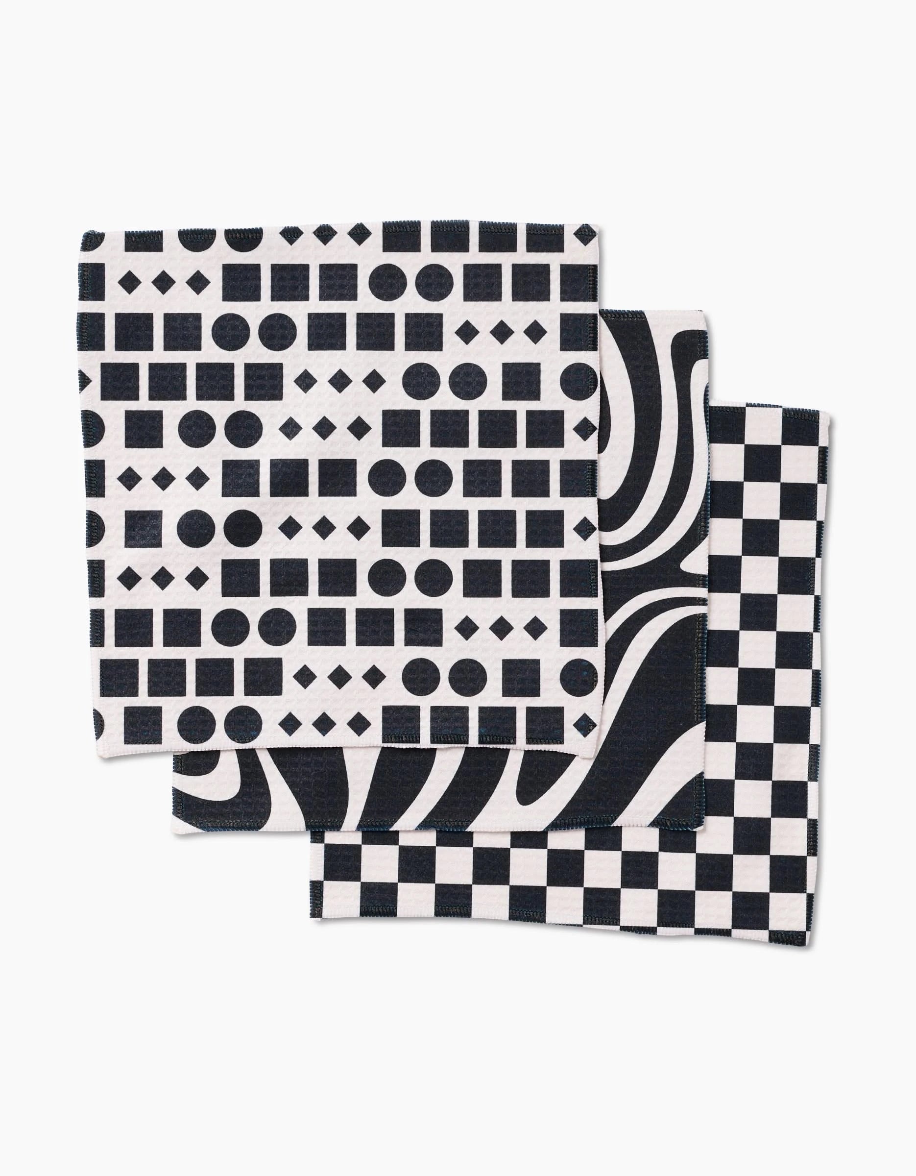 The GEOMETRY Mixed Up set includes three luxe washcloths with bold black and white geometric designs: one with dots, squares, and diamonds; one with wavy lines; and one in a classic checkerboard pattern.