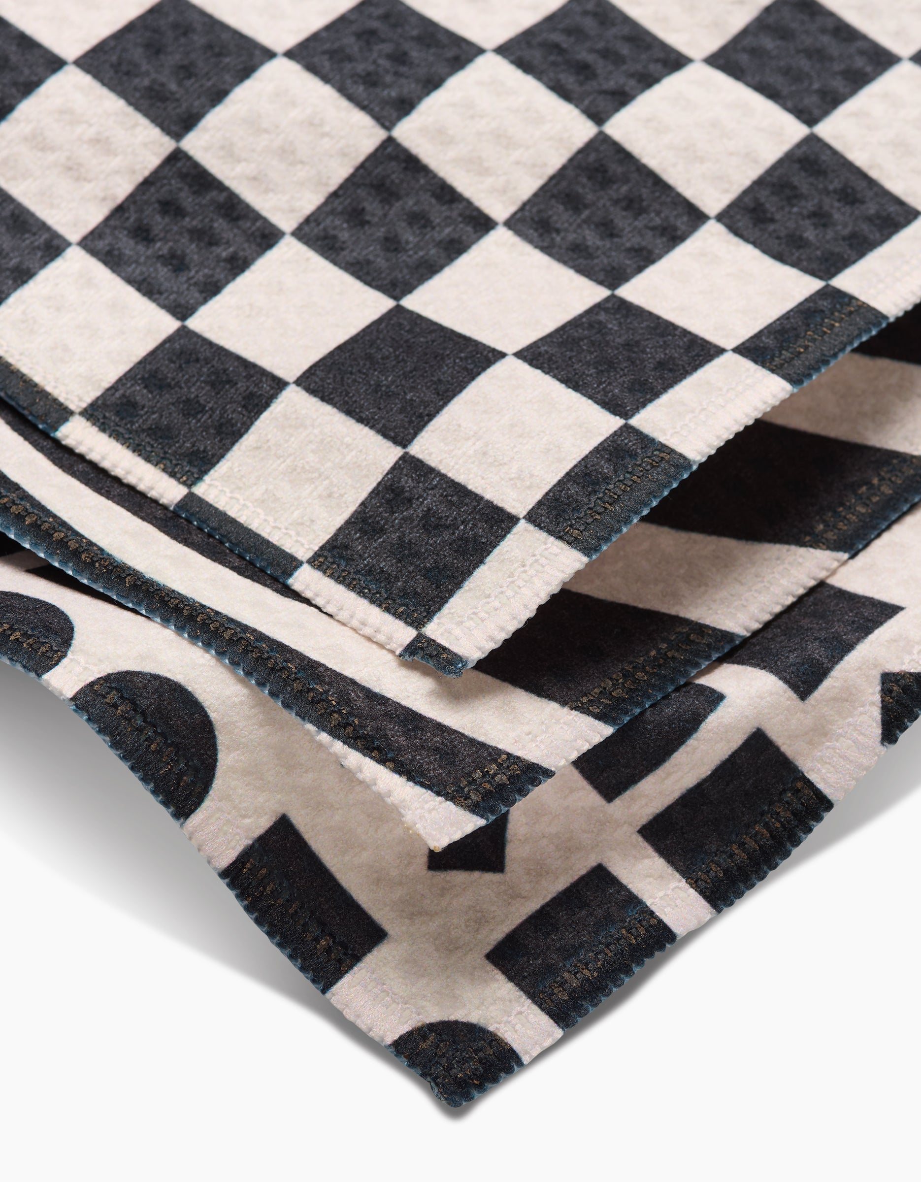 A close-up of GEOMETRYs Mixed Up recycled bath towels stacked together, featuring black and white checkered and geometric patterns that highlight their textured fabric and stitched edges.
