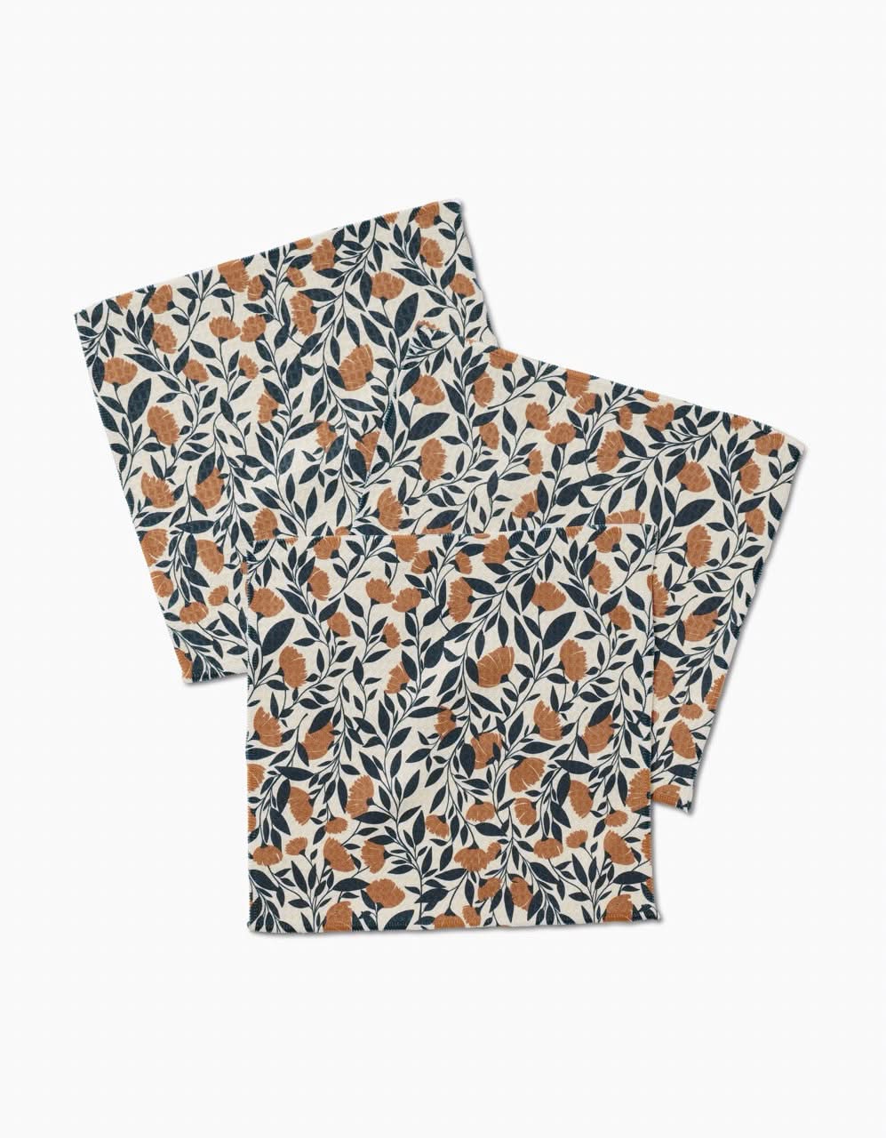 The Naomi napkins by Charlie Rowan Designs feature a botanical pattern with orange leaves and dark blue branches on white, crafted from ultra-absorbent recycled materials. Set includes two folded fabric napkins.