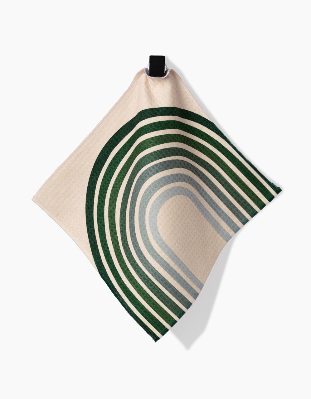 The Olive Arches Luxe Washcloth by GEOMETRY features dark and light green curved stripes on beige, arranged in a rainbow-like pattern. Made with ultra-absorbent Geoweave™ technology, it hangs from a black clip against a white background.