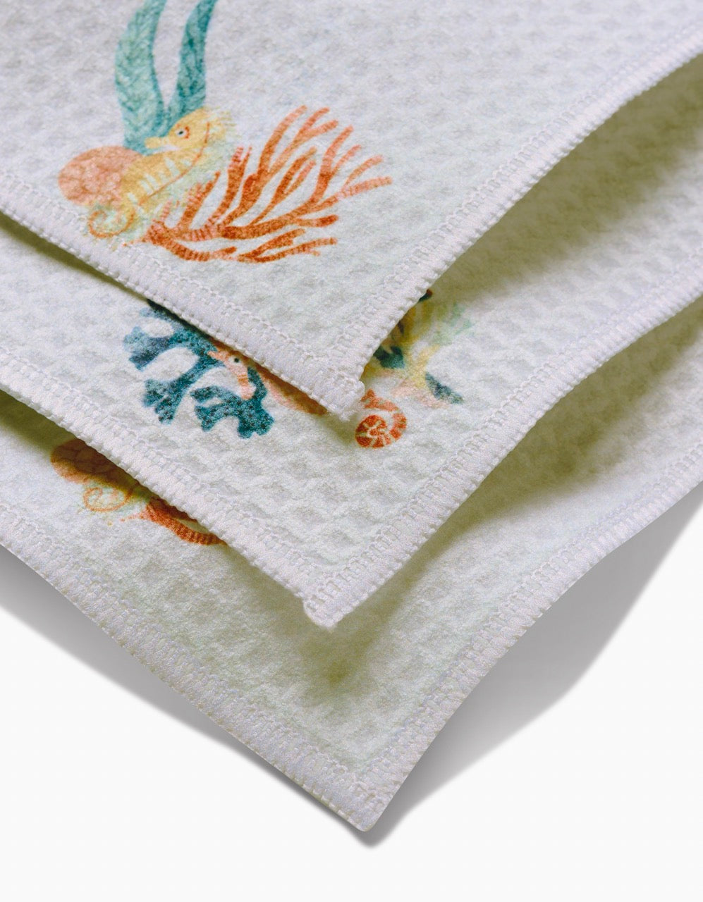 Close-up of three stacked Janna Sue Design Seahorse Serendipity washcloths, featuring a textured waffle pattern and colorful sea-themed coral, seaweed, and shell edges. These ultra-absorbent towels add style and function to any bathroom.