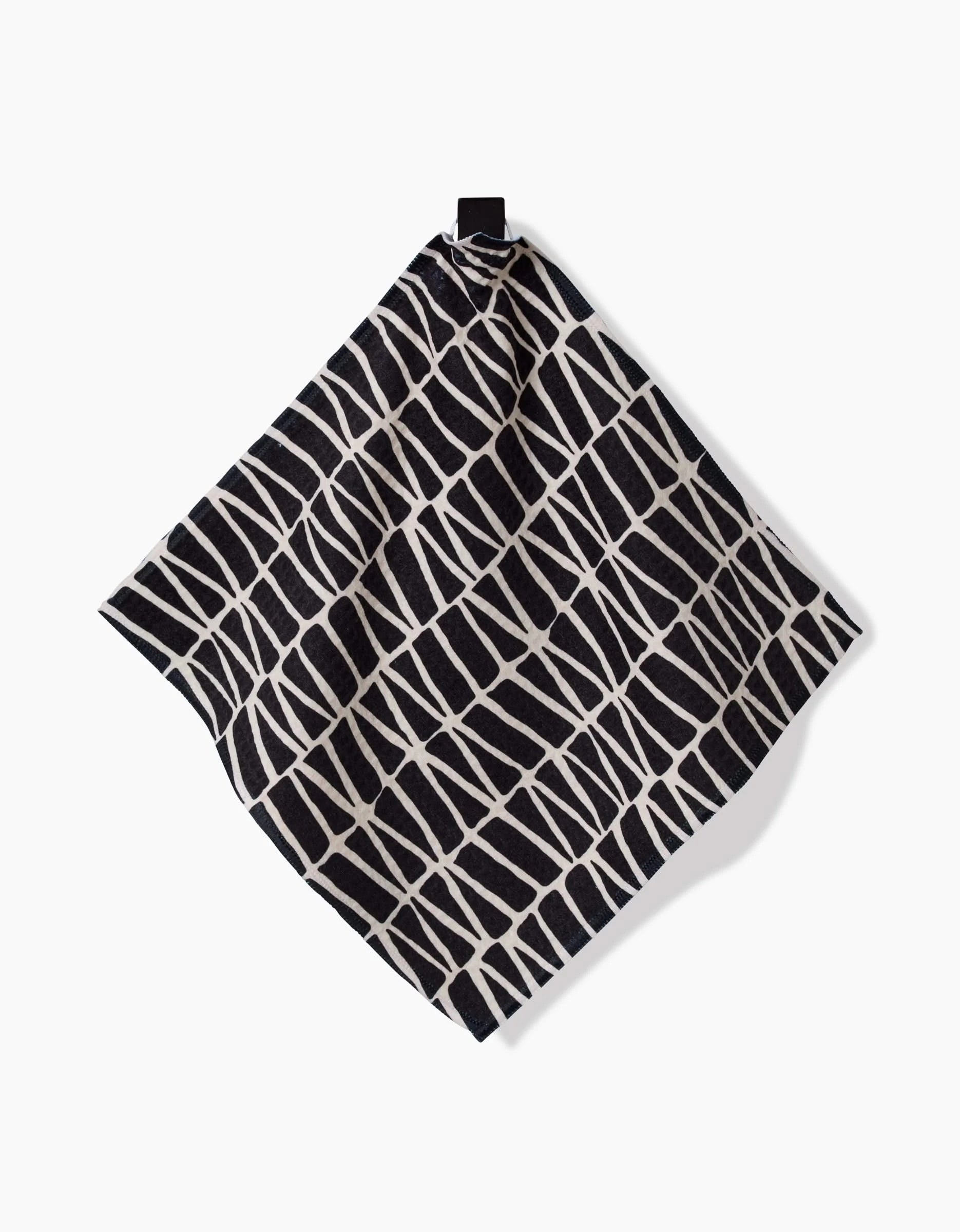 The Rosa Kichline Textured Geometry washcloth, featuring a black and white irregular grid pattern, hangs from a black loop against a plain white background.