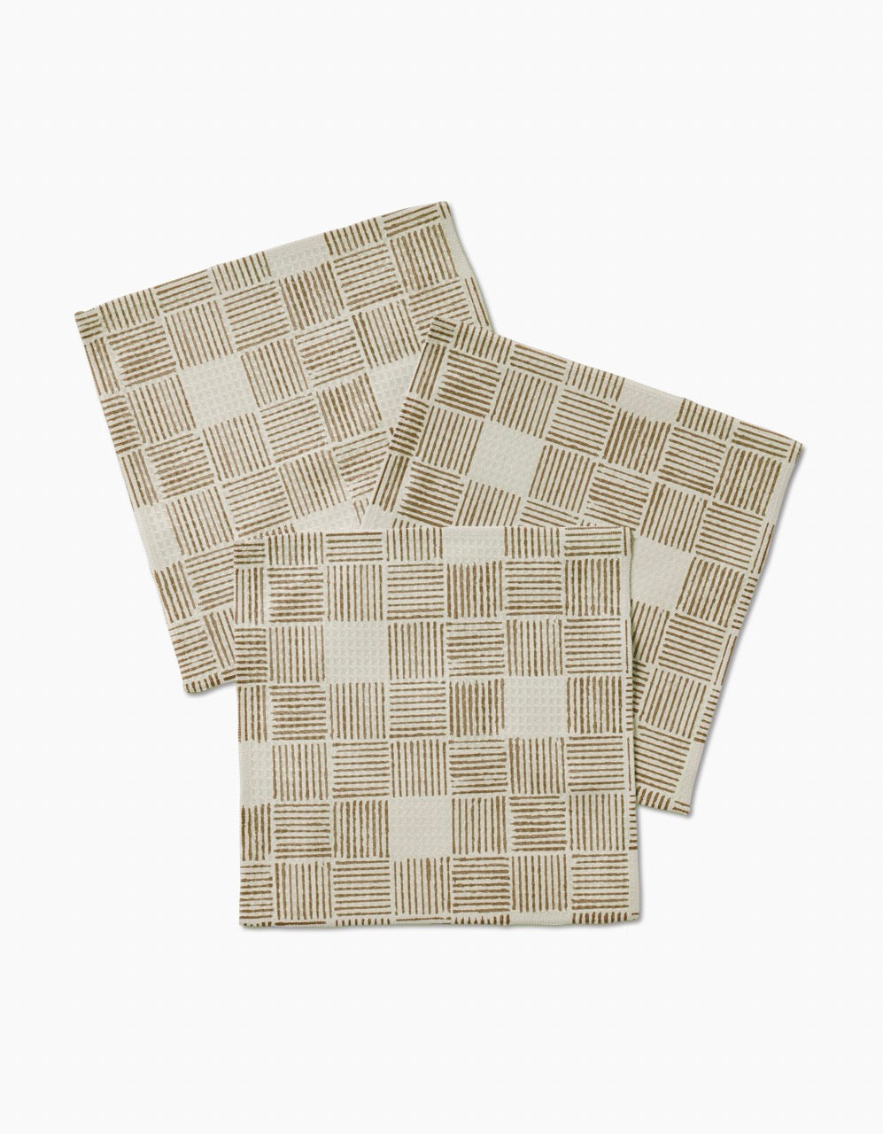 Three Thatcher napkins by Studio Jeannot, featuring a beige color and brown grid pattern, made from ultra-absorbent recycled materials, are arranged overlapping on a white background.