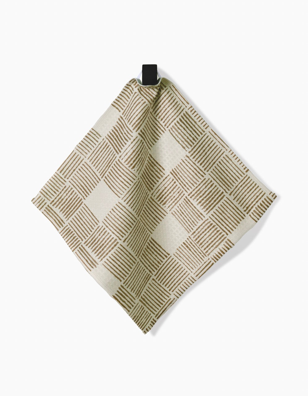 The Studio Jeannot Thatcher dish towel, made from recycled materials in beige and light brown with a geometric checkered pattern, hangs on a black hook against a plain white background.