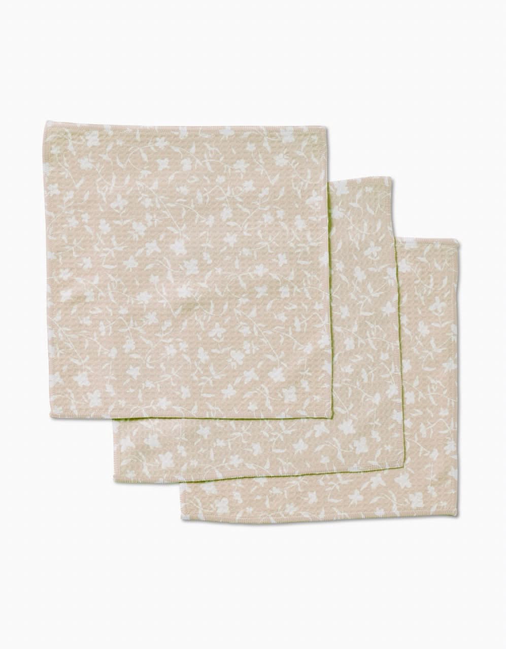 Three beige Tiny Floral cloth napkins by Aubrey Fairchild, featuring a subtle white floral pattern and crafted with ultra-absorbent Geoweave technology, are neatly stacked on a plain white background.