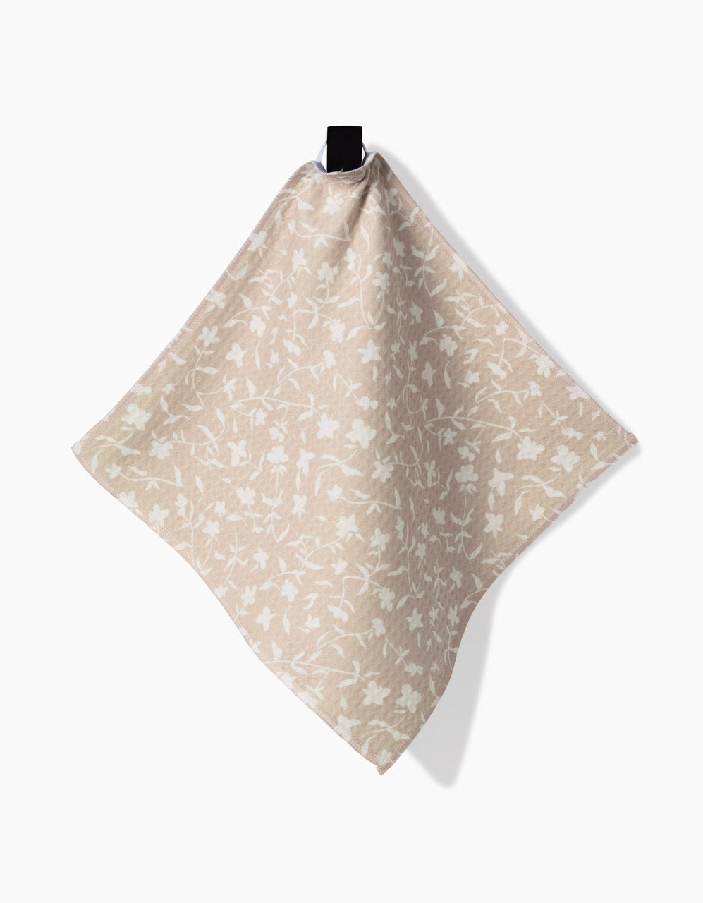Aubrey Fairchilds Tiny Floral washcloth napkin in square beige features a subtle white floral pattern and hangs from a black clip against a white background, highlighting its ultra-absorbent performance.