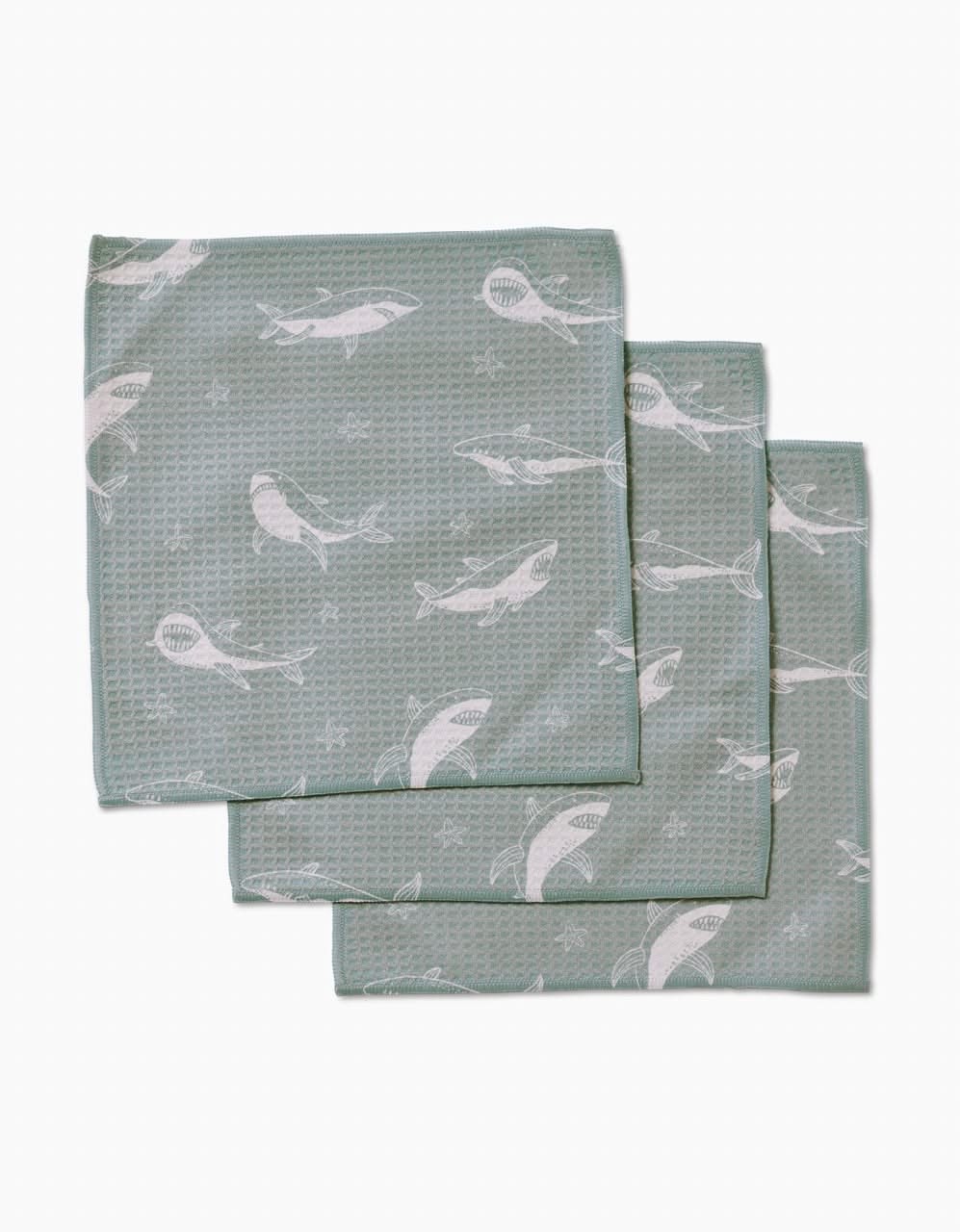 Three folded Toothy Tales washcloths by Janna Sue Design, in green with a textured surface and white whale pattern, are stacked with slight overlap on a plain white background. Made from recycled materials, theyre ultra-absorbent and eco-friendly.