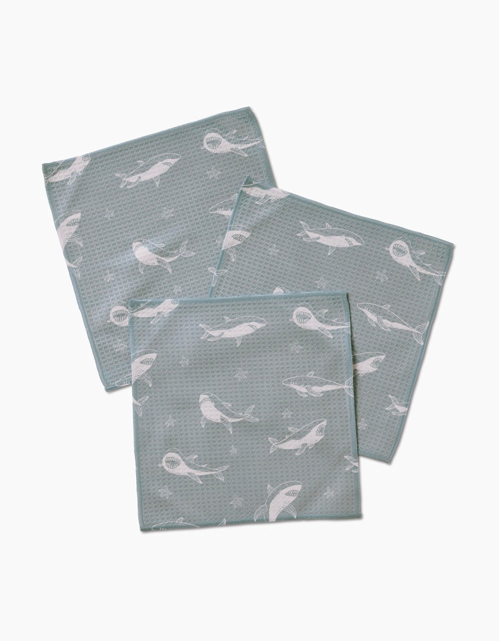 Three ultra-absorbent light blue Toothy Tales washcloths by Janna Sue Design, featuring a white whale and bubble print, are arranged in an overlapping pattern on a plain white background.