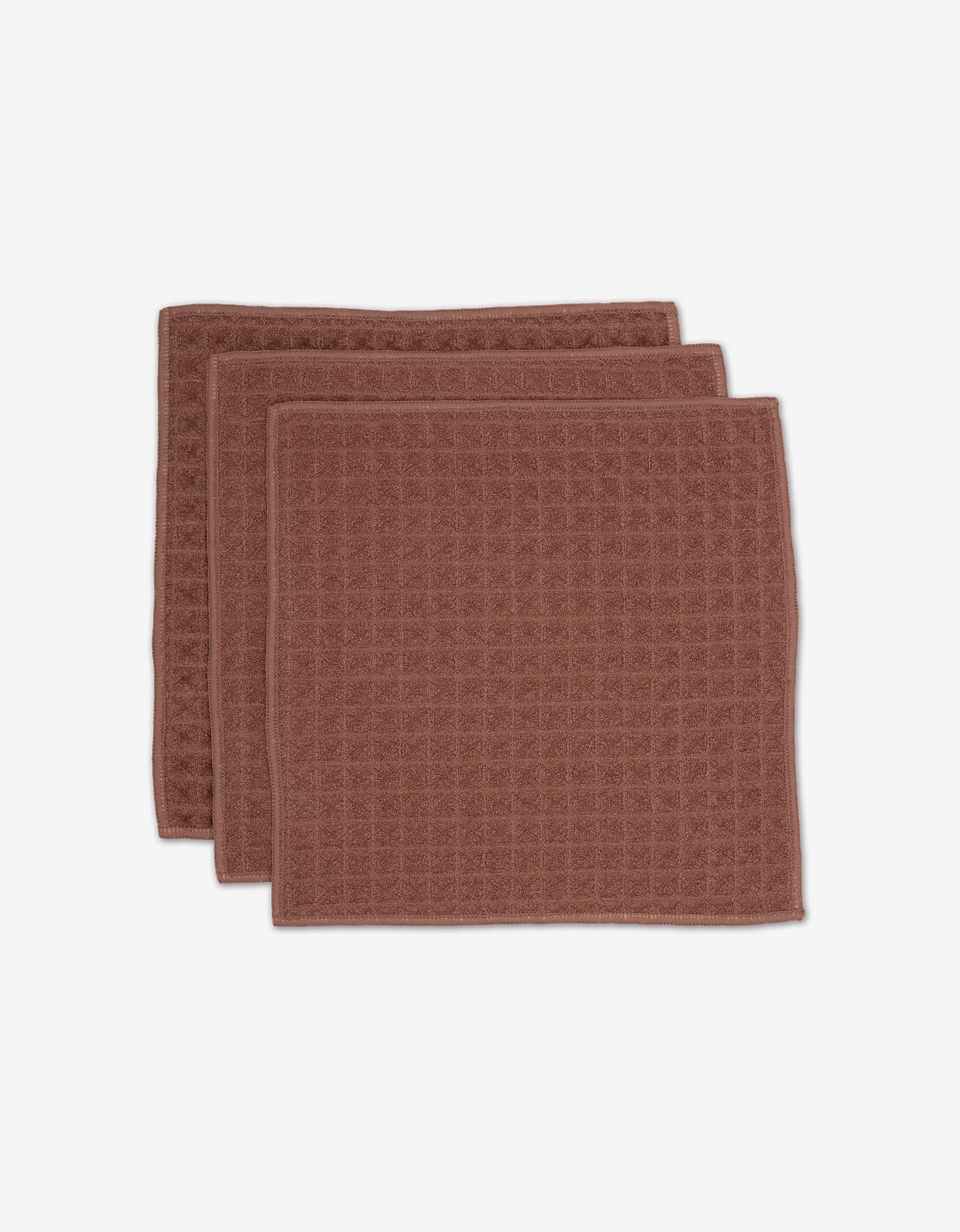 Three dusty rose waffle-textured cloths from GEOMETRY are neatly stacked with slight overlap against a white background.