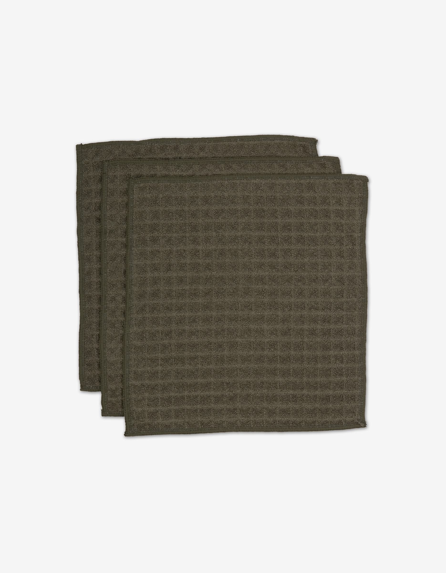 Three Forest cloths by GEOMETRY in dark green with a waffle texture, made from recycled materials, are stacked slightly offset on a white background.