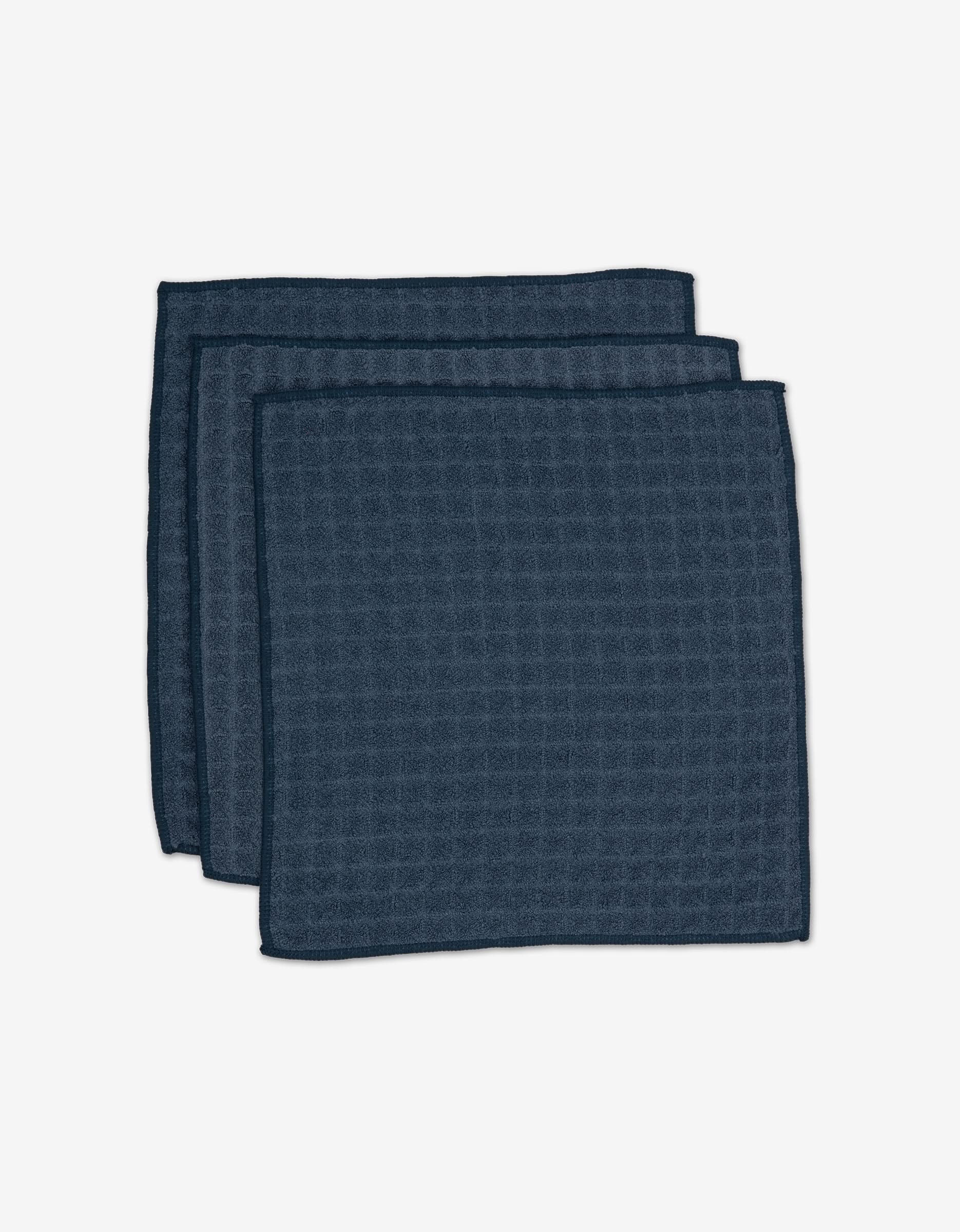 Three folded GEOMETRY Midnight Blue Waffle Washcloths with a subtle waffle texture, stacked and slightly overlapping on a white background.