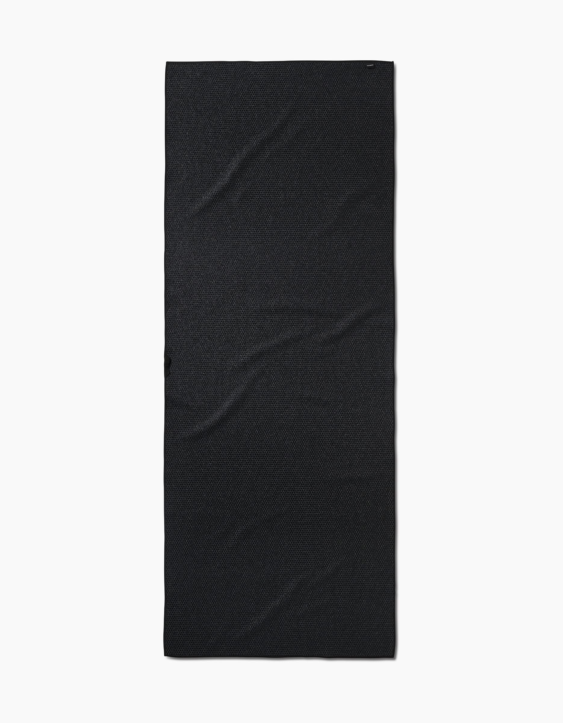 A rectangular black yoga towel named Foundation lies flat on a white background, displaying subtle creases and texture, crafted from recycled materials.
