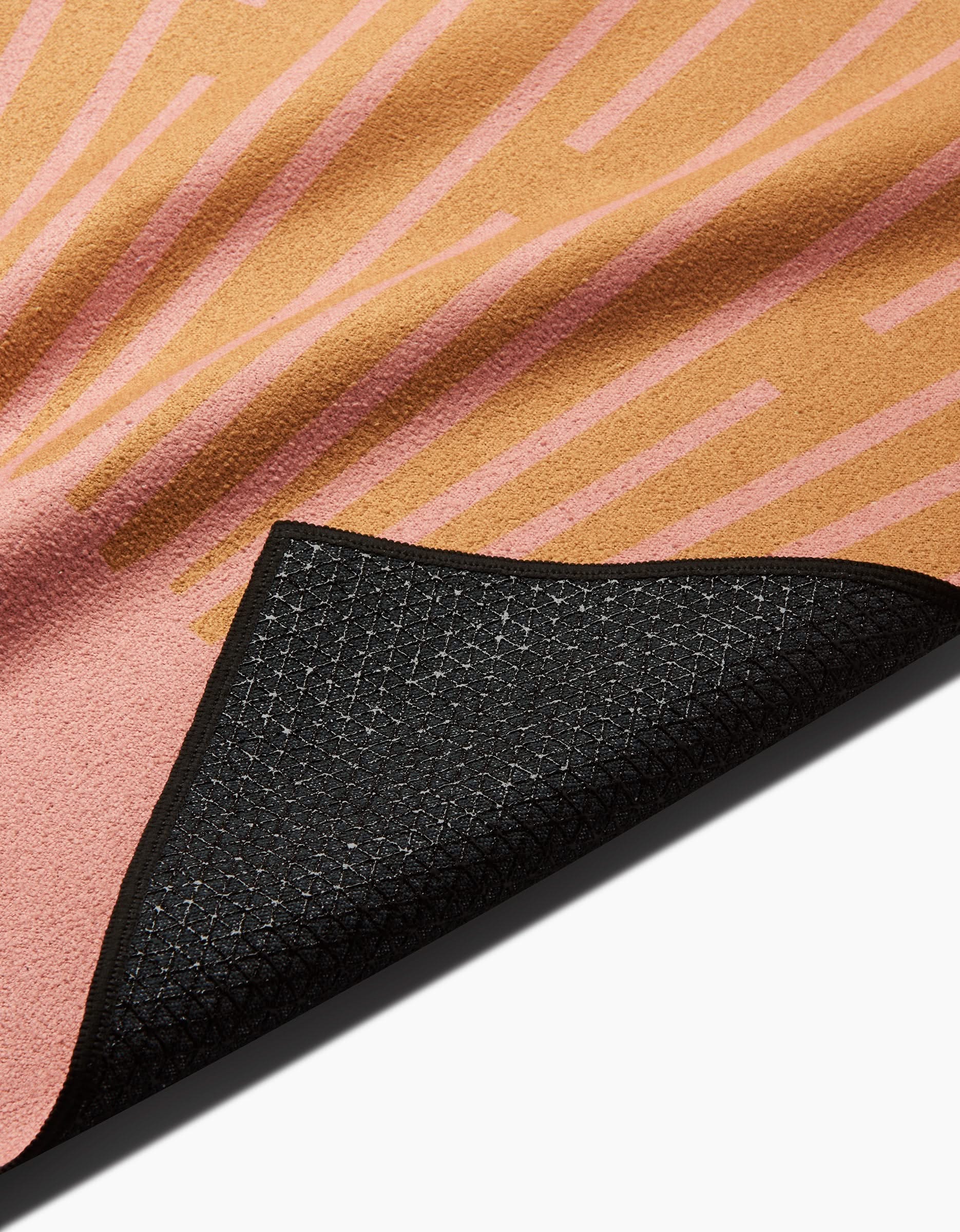 A close-up of the Arielle Estoria Love and Acceptance Affirmation yoga mat, featuring a pink and tan geometric design on top and a black textured slip-resistant underside, partially folded to display both sides, made from recycled materials.