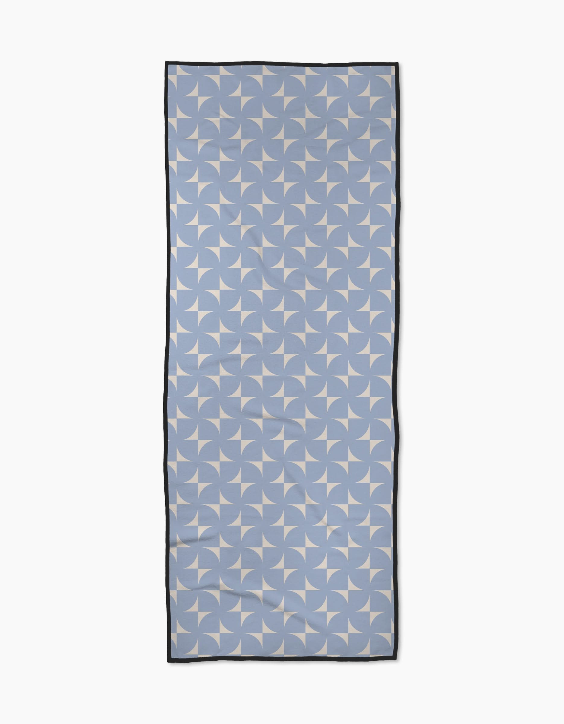 The Airy Flow scarf by Geometry is rectangular and light blue, made from recycled materials with a white geometric pinwheel pattern and thin black border, shown laid flat on a white background.