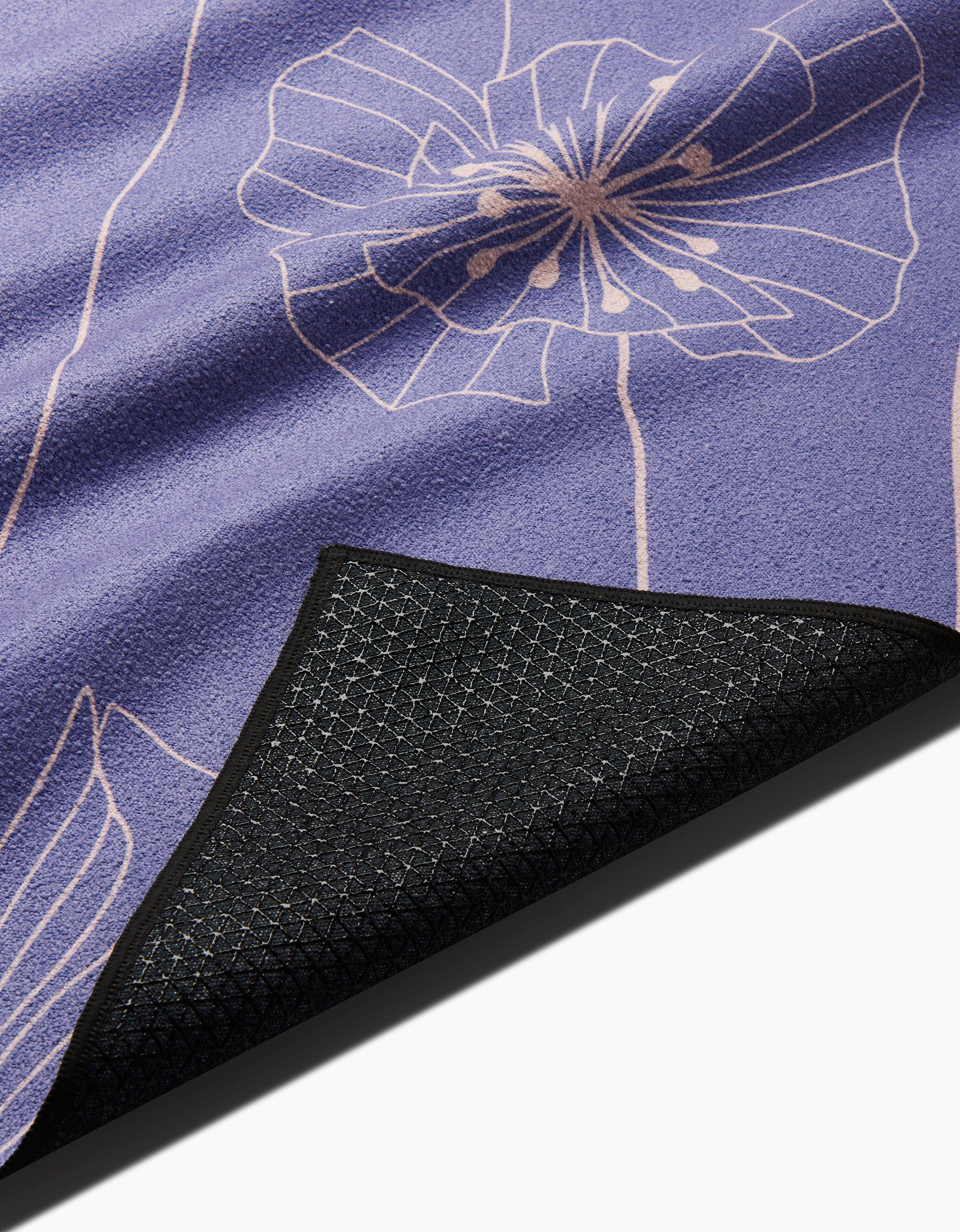 A close-up of the GEOMETRY Alexa mat shows its purple surface with a white floral line design; one corner is flipped to display the textured black silicone grip underside for stability.