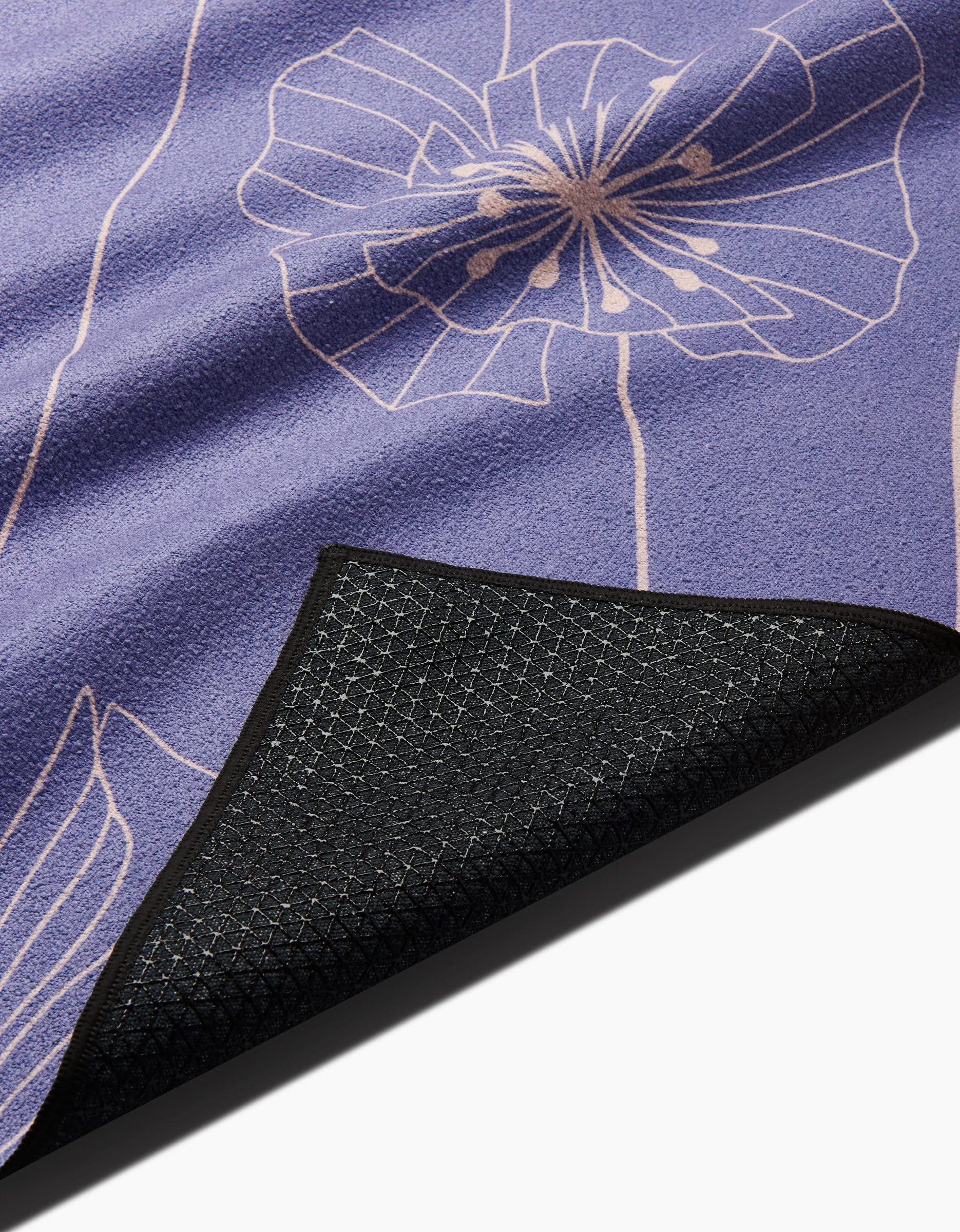 A close-up of the GEOMETRY Alexa mat shows its purple surface with a white floral line design; one corner is flipped to display the textured black silicone grip underside for stability.