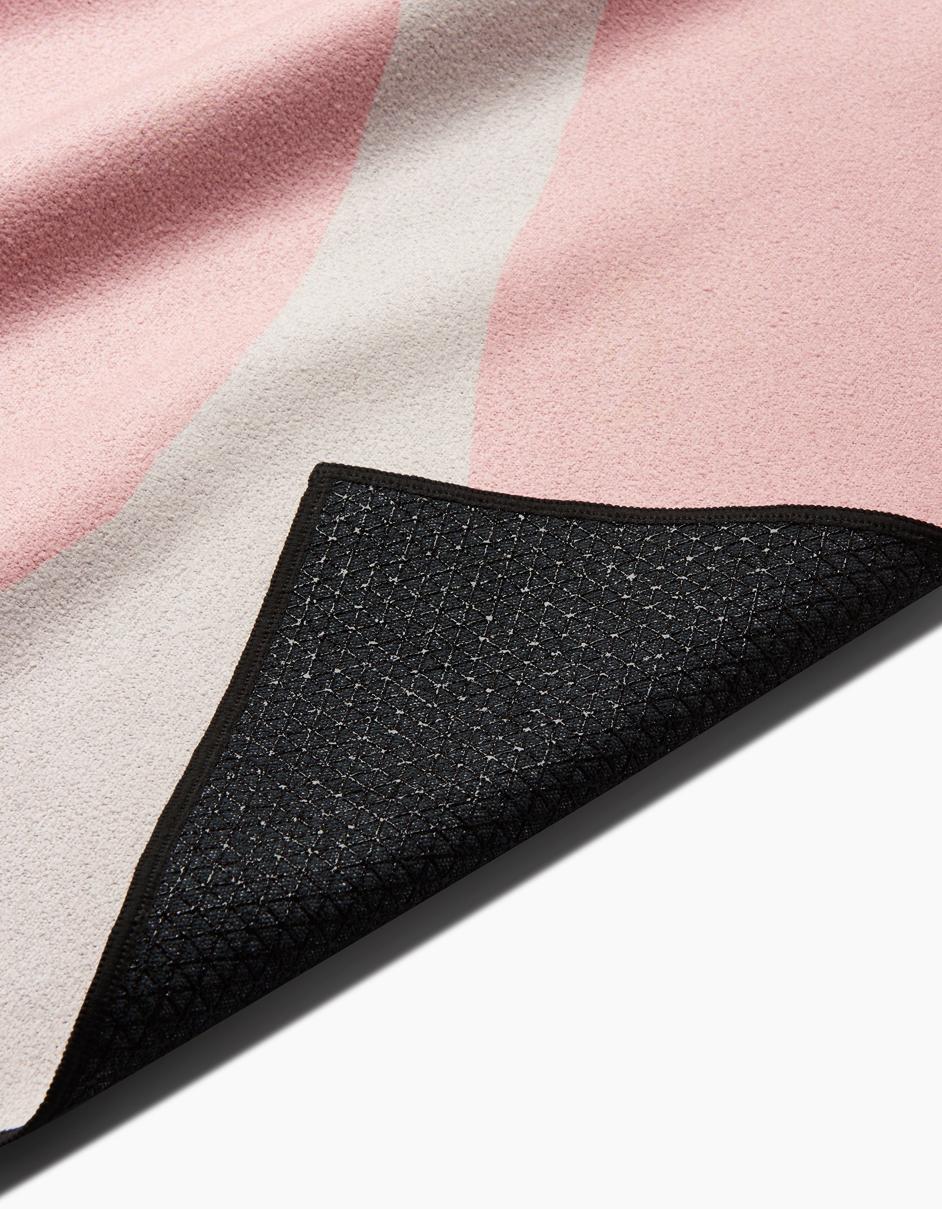 A close-up of GEOMETRYs Bare yoga towel shows its soft pink and beige top surface with a black, textured, non-slip underside; one corner is flipped to display both sides of this silicone grip yoga towel.