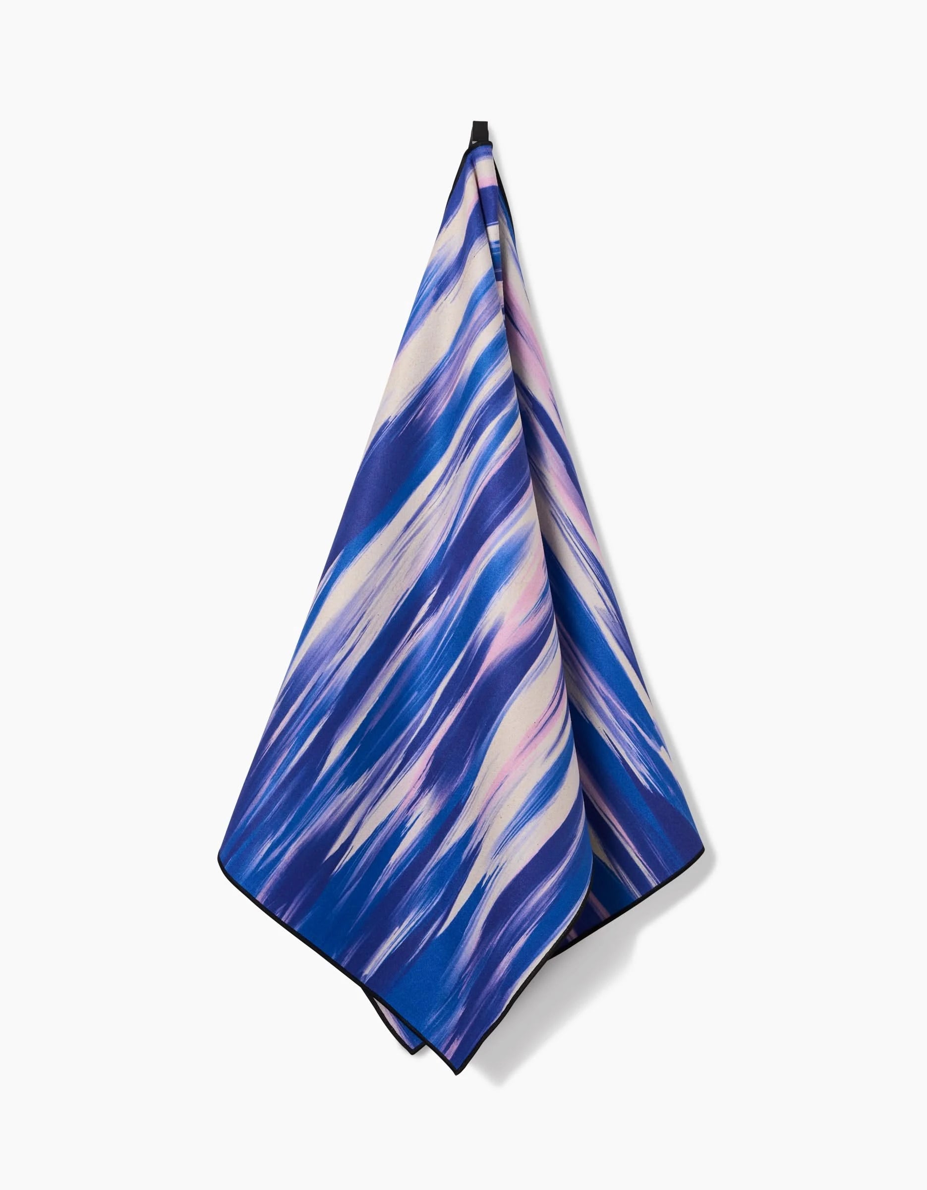 The GEOMETRY Blue Blast yoga towel, featuring an abstract blue, purple, and white wavy design, hangs from a point against a plain white background.