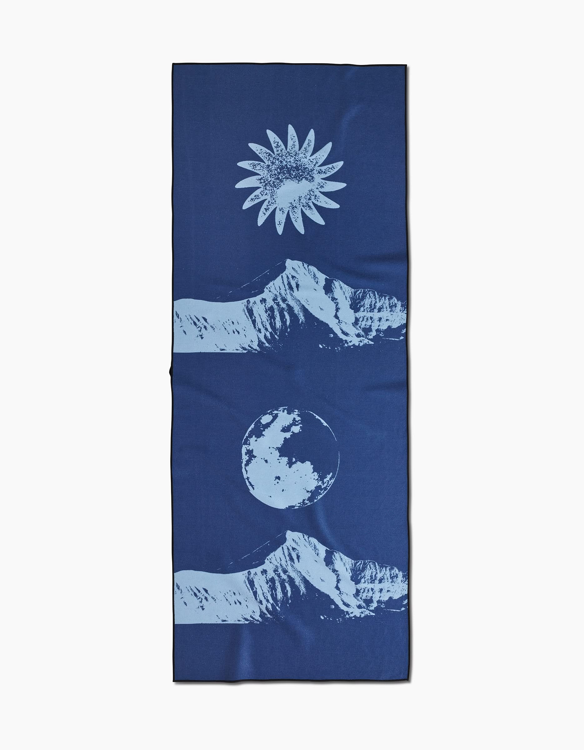 The Blue Moon yoga towel by Graphics and Grain is a blue, rectangular, slip-resistant towel with light blue mountain illustrations, a sun at the top, and a moon at the bottom—all arranged vertically on a plain background.