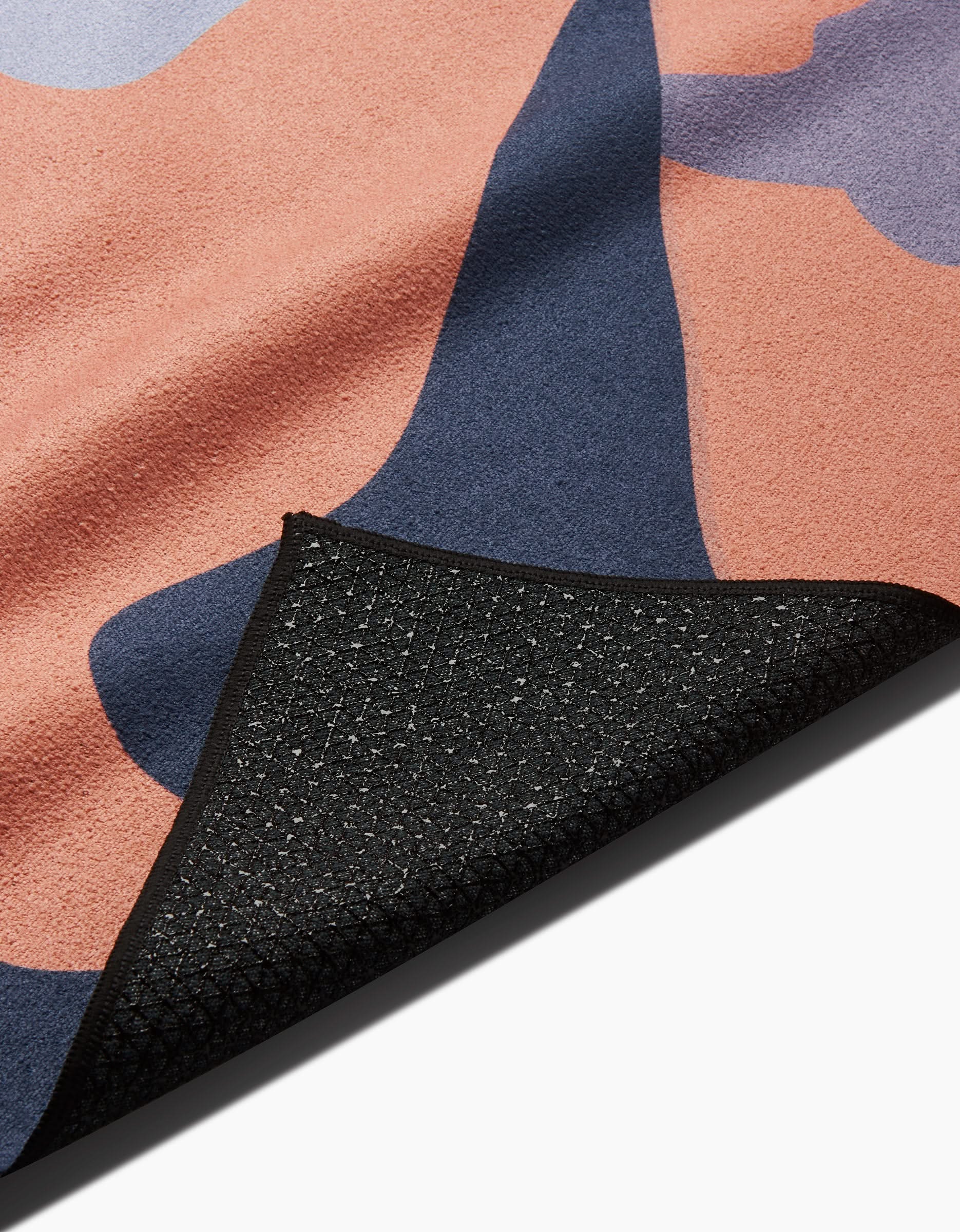 A close-up of the GEOMETRY Camo yoga mat with a pink and navy abstract pattern, showing its black textured, slip-resistant towel underside and part of the mat folded over.