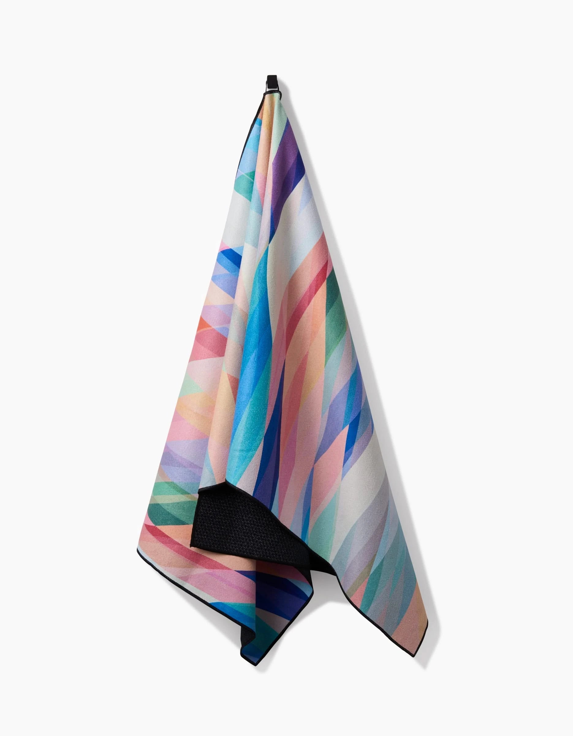 The Eventide yoga towel by Rachel Parker features an abstract geometric pattern in blue, pink, green, and purple. Made from recycled materials, it hangs on a hook against a plain white background.