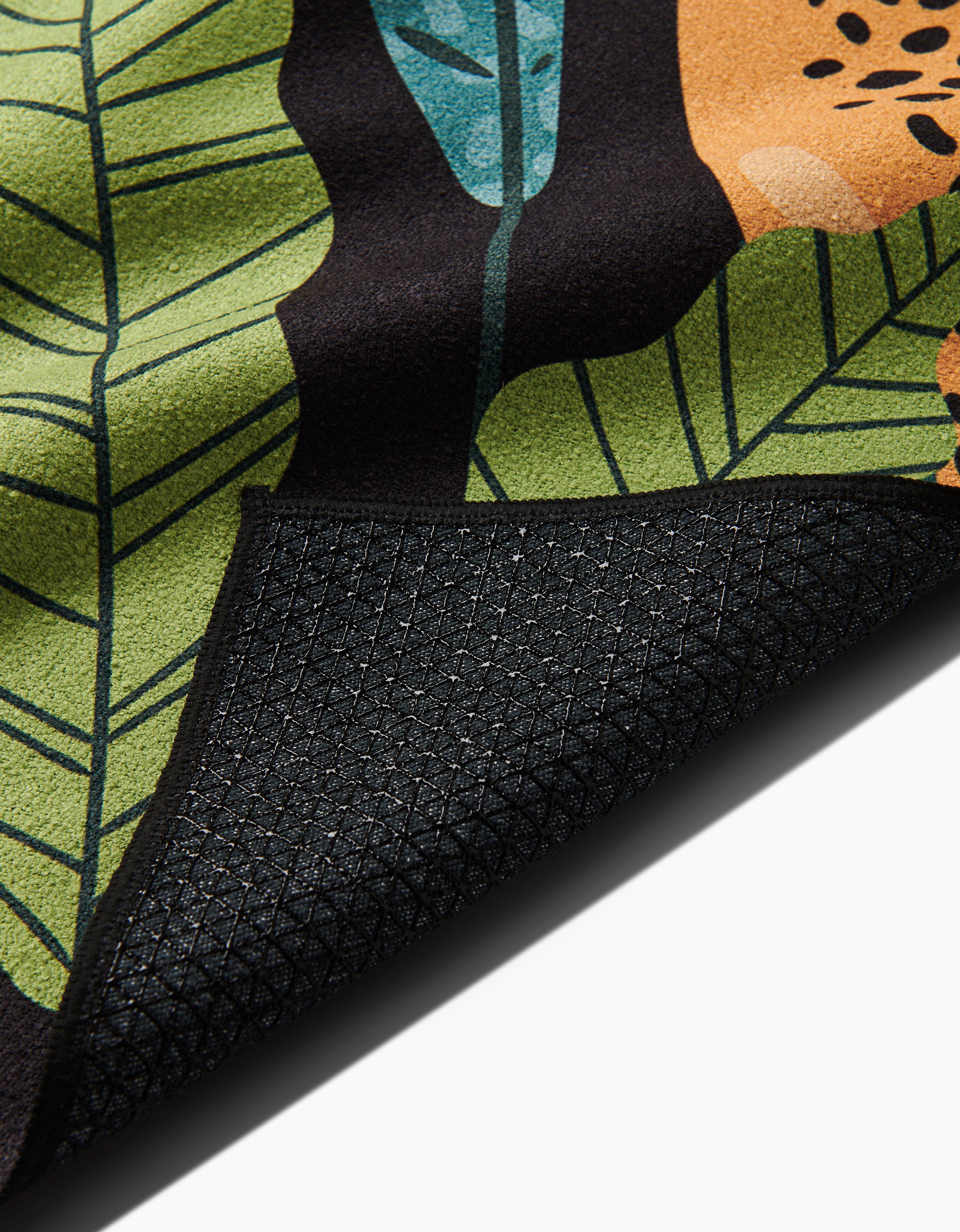 A close-up of the GEOMETRY Feeling Spotty mat, featuring a colorful leafy pattern and a black, textured slip-resistant backing, with one corner folded over to display the underside.