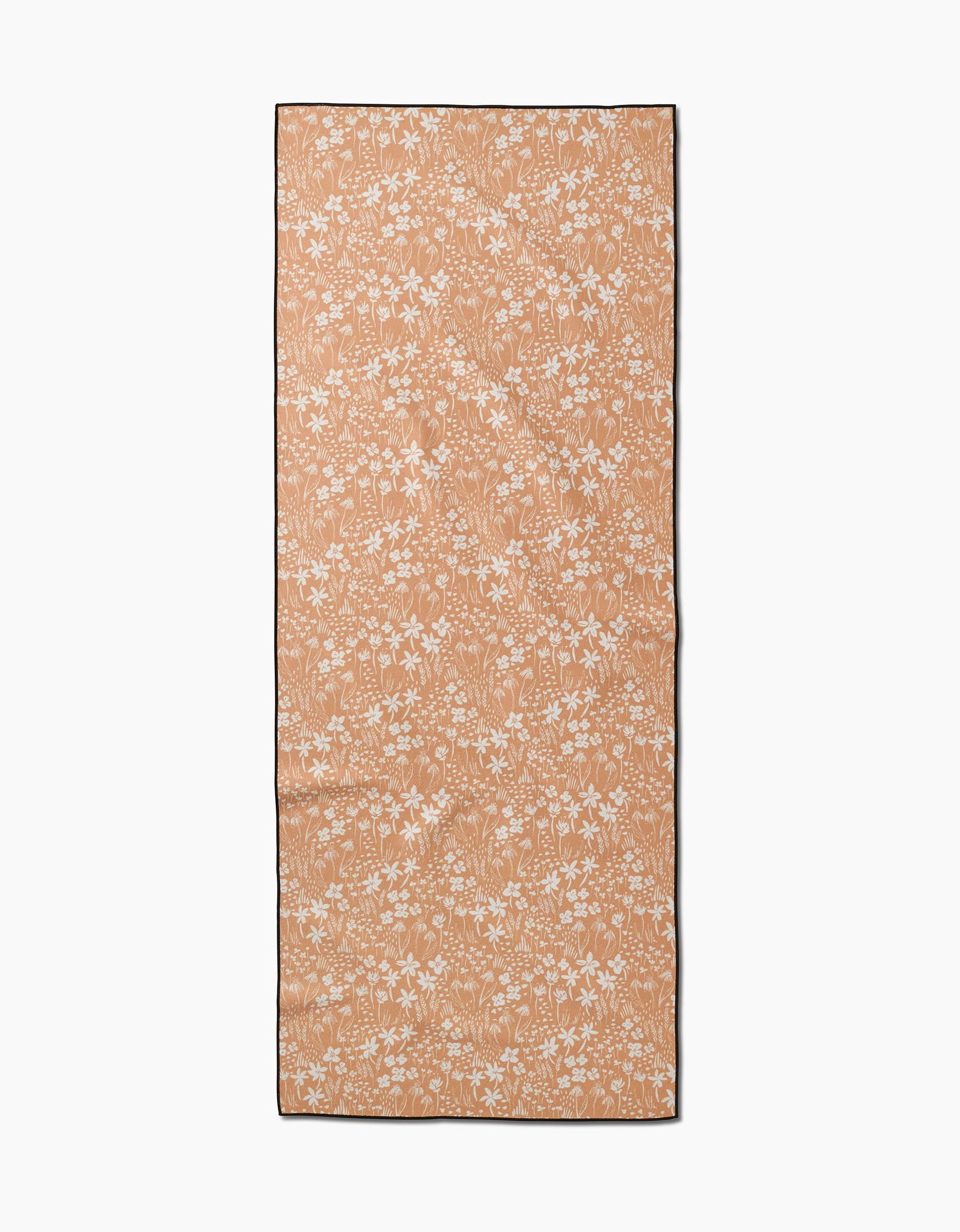The Floating Meadow yoga towel by Hufton Studio features a tan, slip-resistant surface with a white floral pattern and dark border, shown flat on a white background.