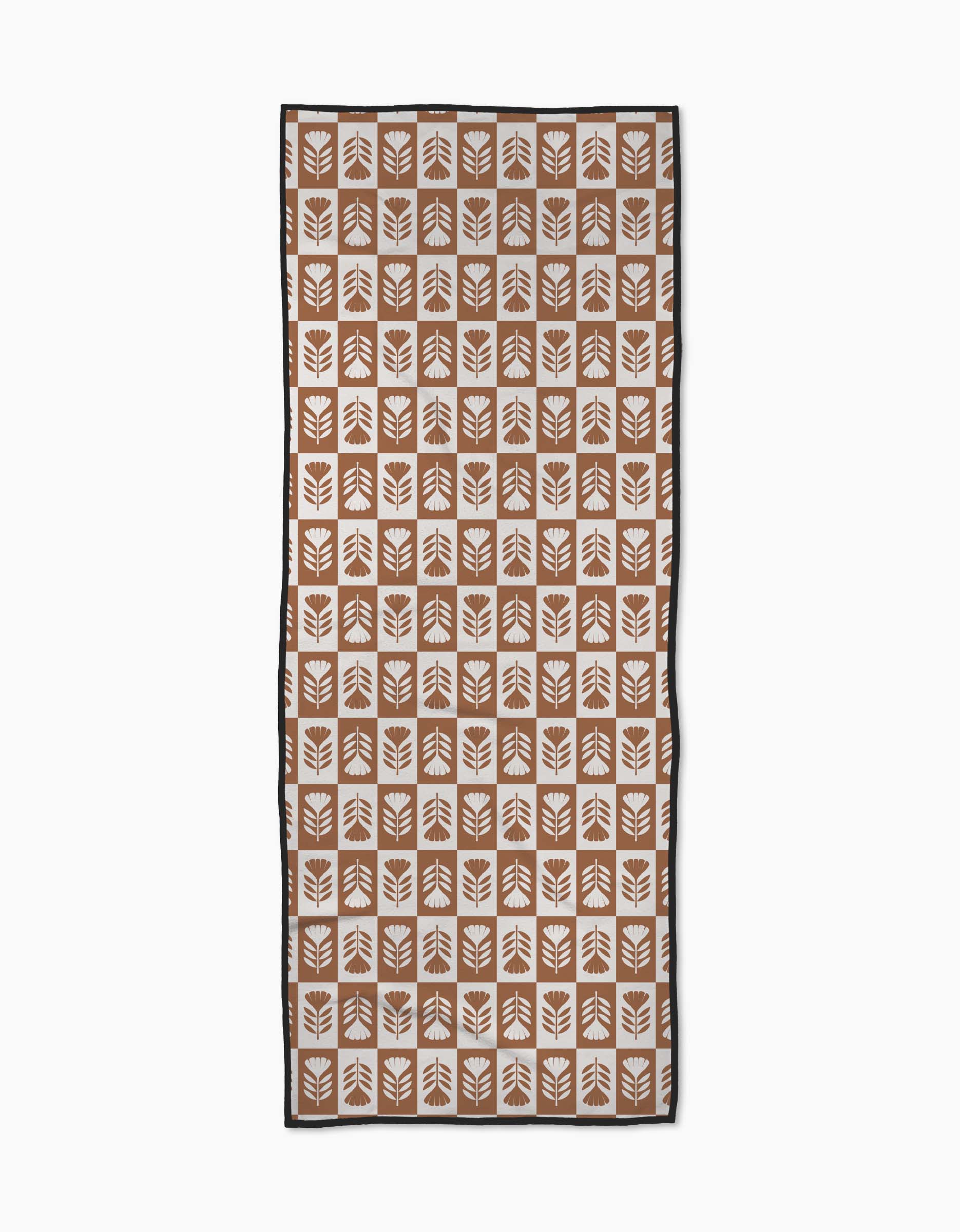 The Flower Patch yoga towel by Charlie Rowan Designs features a symmetrical geometric leaf pattern in brown and white squares with a thin black border and slip-resistant backing.