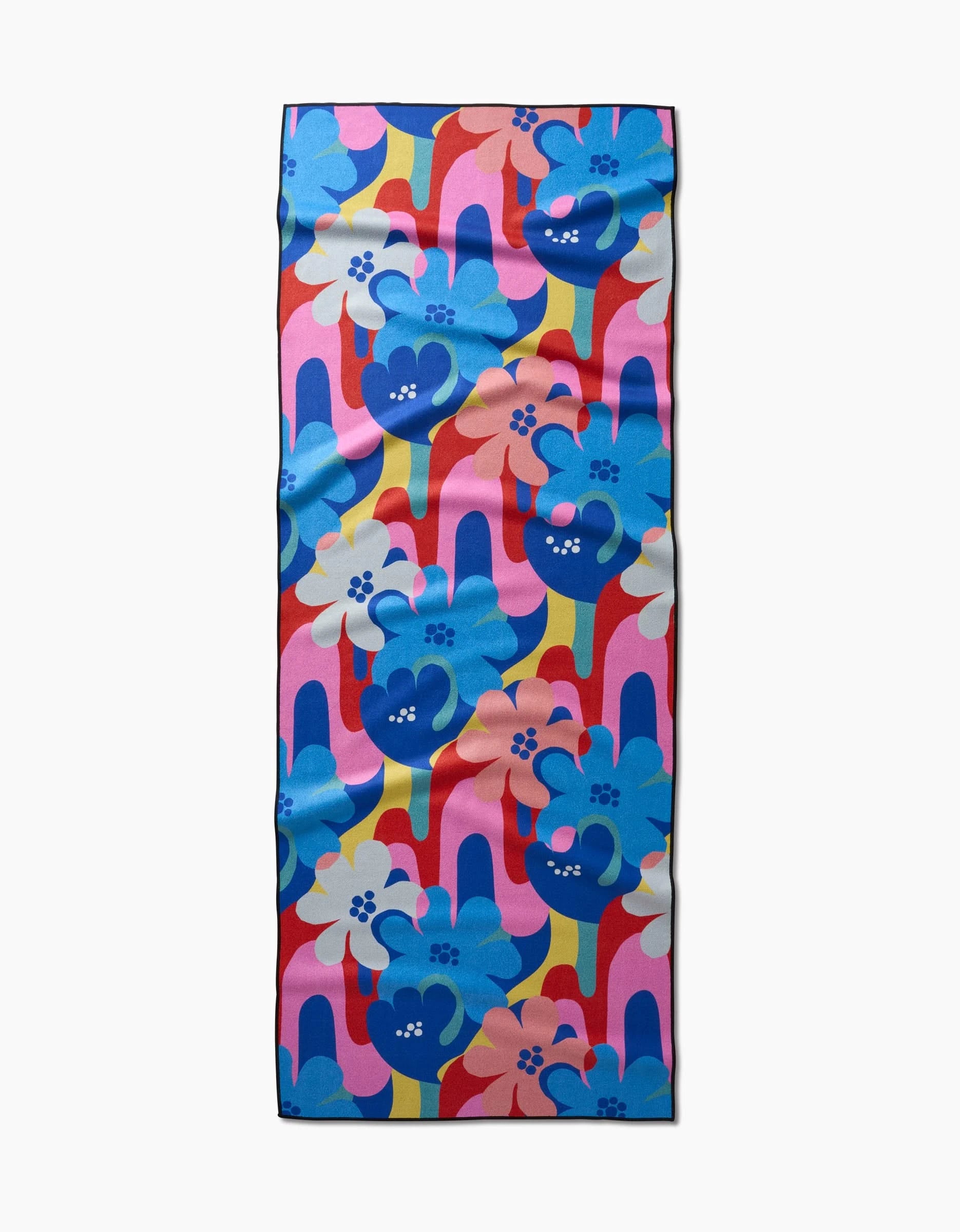 The Flower Powers yoga towel by Masha Volnova features bold blue, pink, red, and yellow retro floral patterns with large flowers and wavy lines on a white background plus a lightly wrinkled texture.
