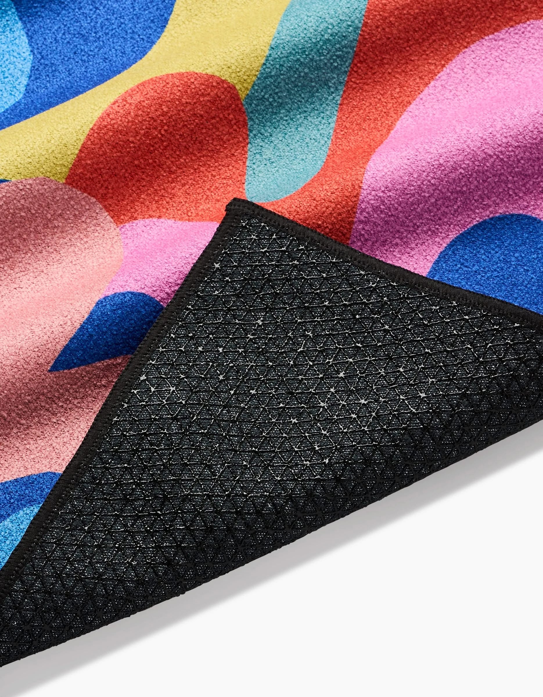 A close-up of the Flower Powers yoga towel by Masha Volnova, featuring a colorful abstract design and a black textured non-slip silicone grip backing, partially folded over.
