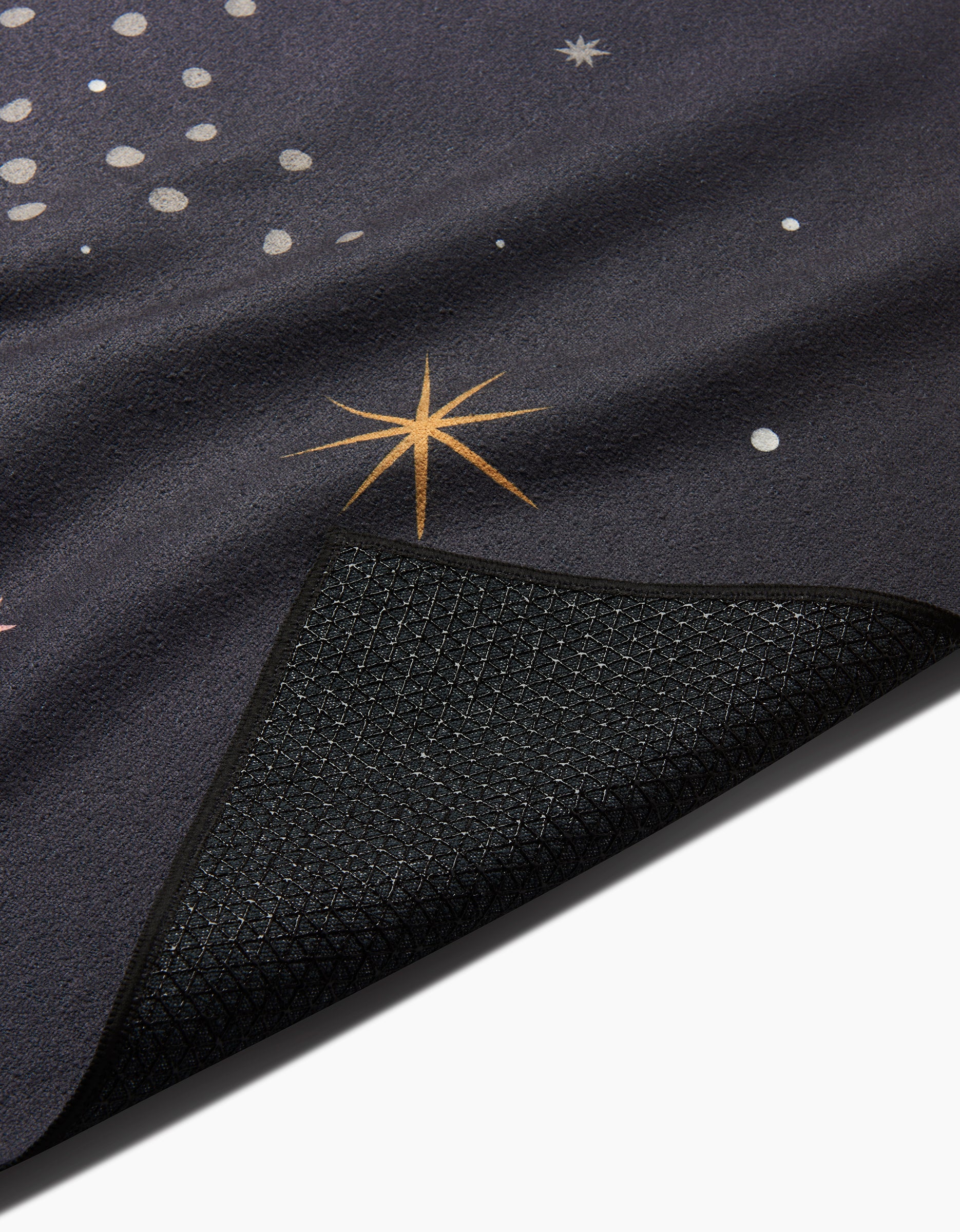 A close-up of Ash Cascade’s Galaxy Burst yoga mat features star and dot patterns, with a corner flipped to reveal its textured black, nonslip underside—ideal for use with your favorite non-slip yoga towel.