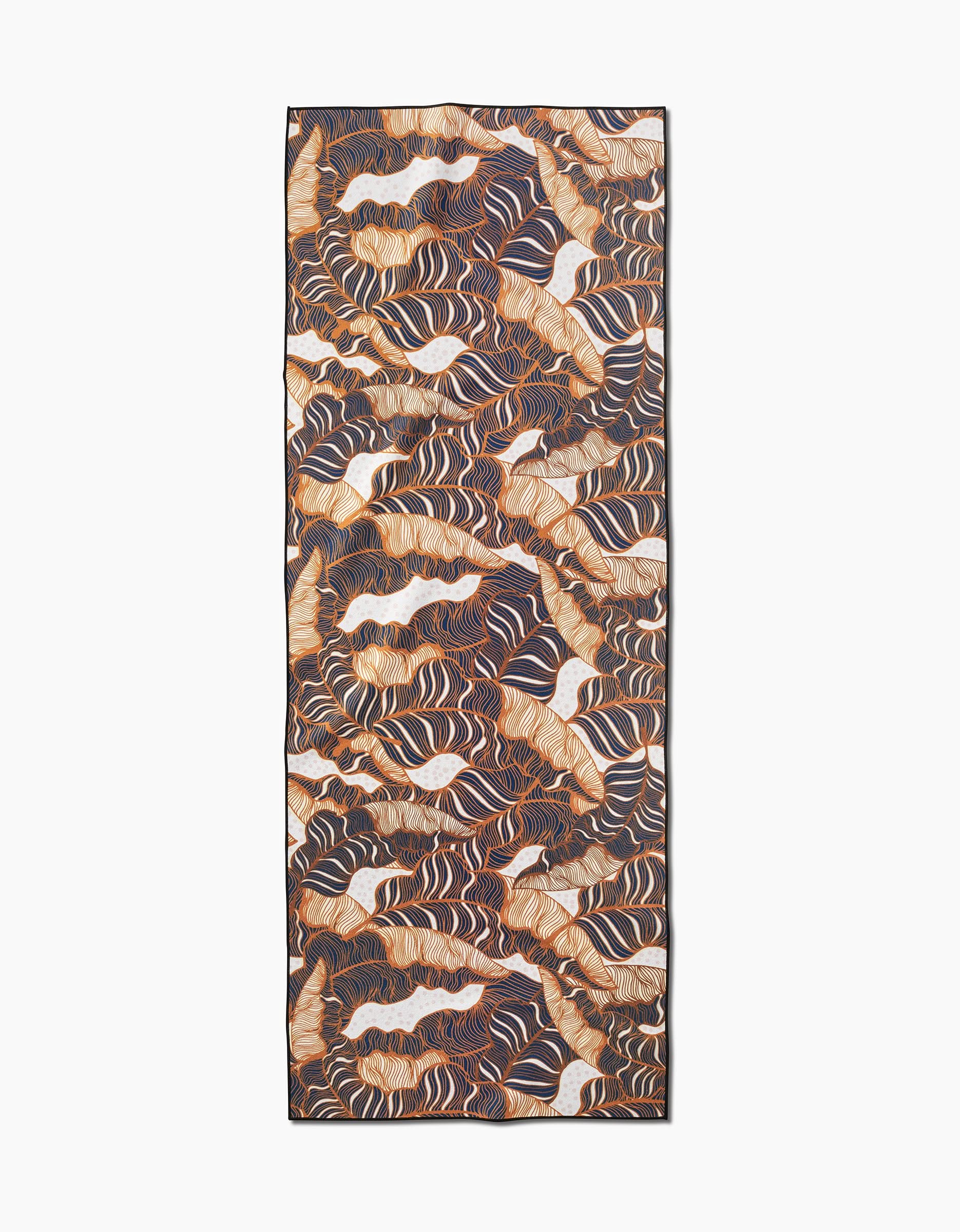 The Golden Palms scarf by Marina Solodka showcases an abstract design with wavy lines in brown, orange, cream, and black. Made from recycled yoga towel-inspired fabric, it has a thin black border for a sustainable touch.