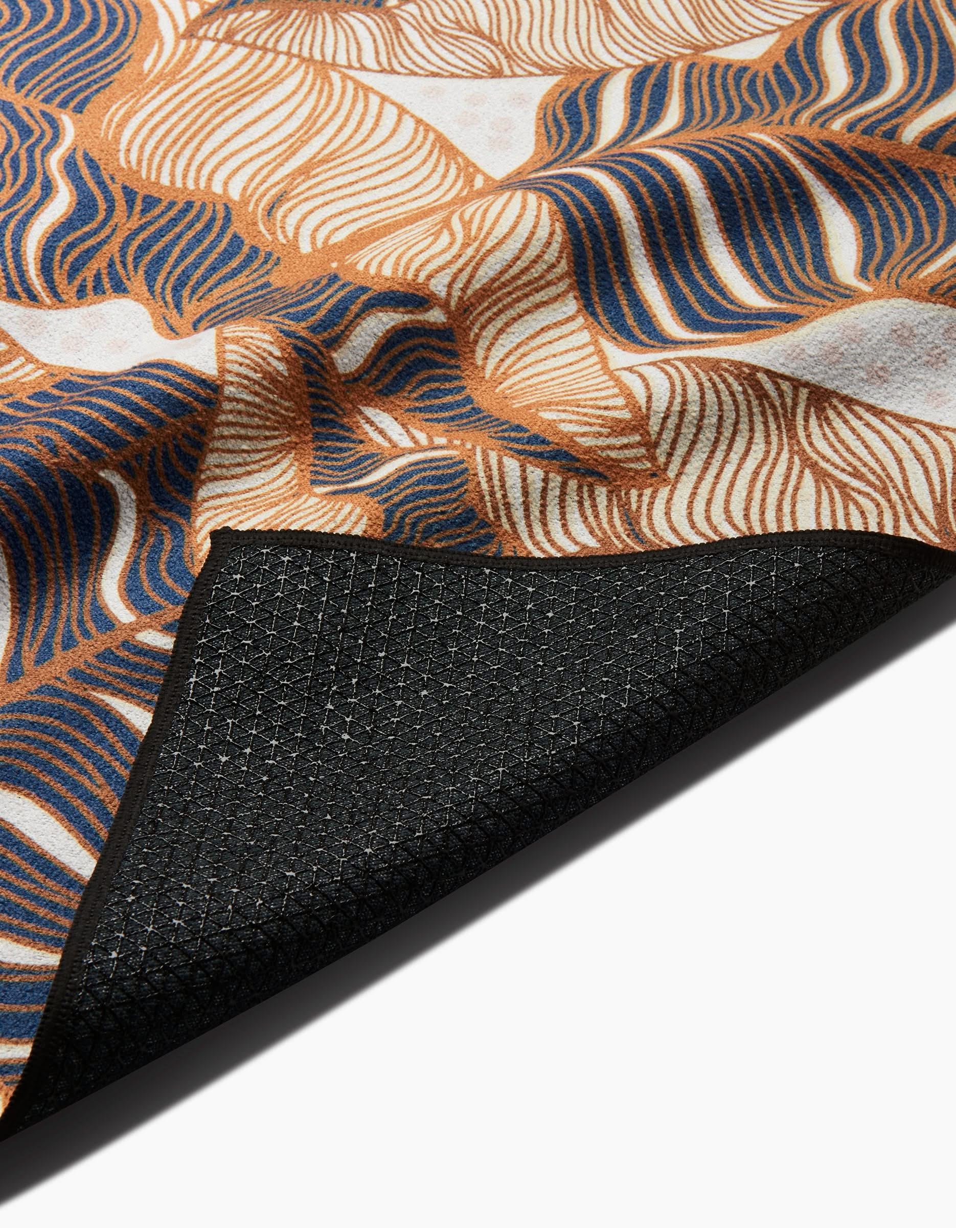 A close-up of the Golden Palms yoga towel by Marina Solodka, with brown, blue, and white wavy lines and a black textured slip-resistant backing partially folded over.