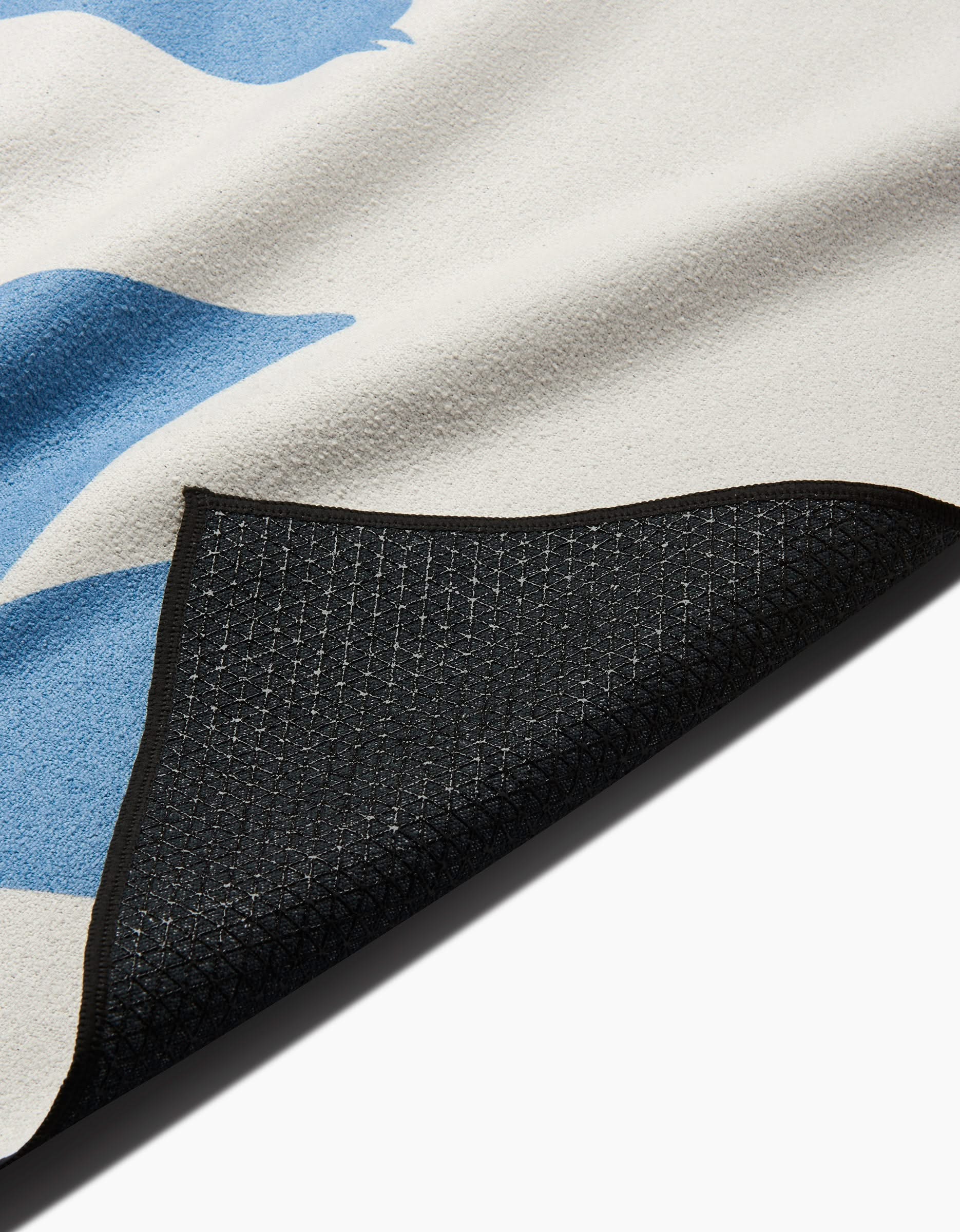 A close-up of the Good Day yoga towel by Quotes by Christie, made from recycled materials with a black grid-patterned silicone grip underside and a white top with light blue shapes, one corner folded to show the backing.
