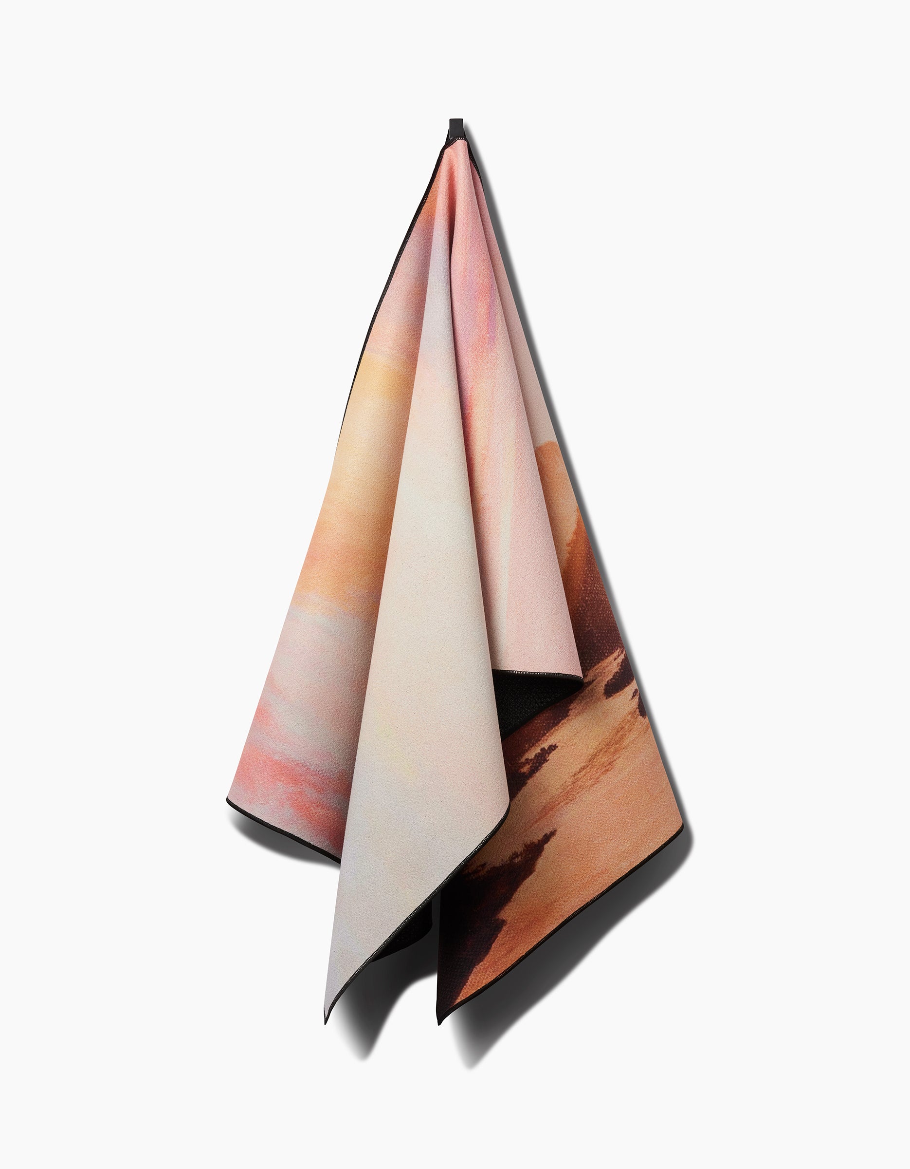 The Her Majesty yoga towel by Stefanie Bales features a warm landscape design in orange, pink, and beige tones. Made from recycled materials, it is shown hanging against a plain white background.