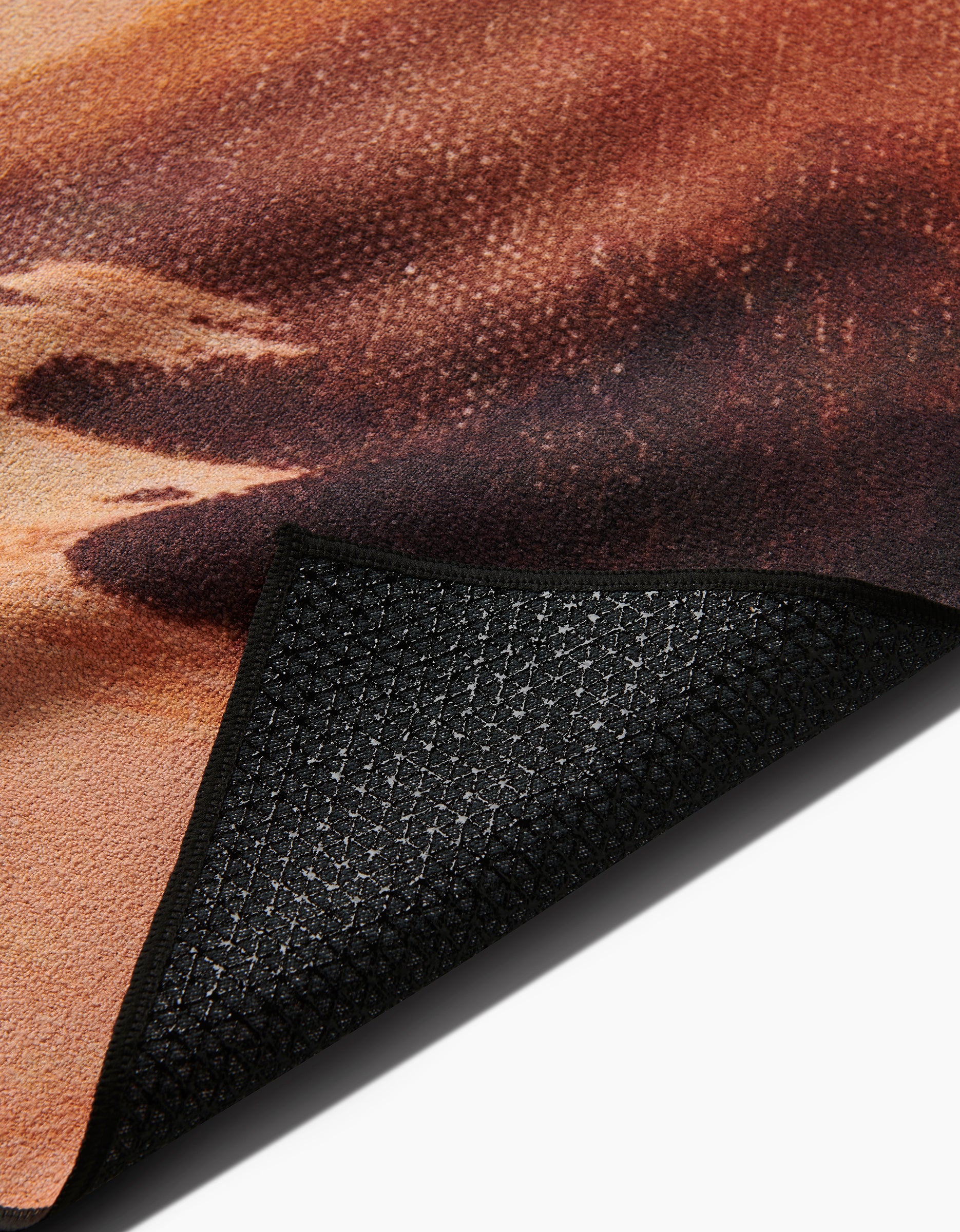 Close-up of the Her Majesty mat by Stefanie Bales, featuring a soft, patterned surface in warm browns, oranges, and beige made from recycled materials, with detailed black slip-resistant backing partially visible.