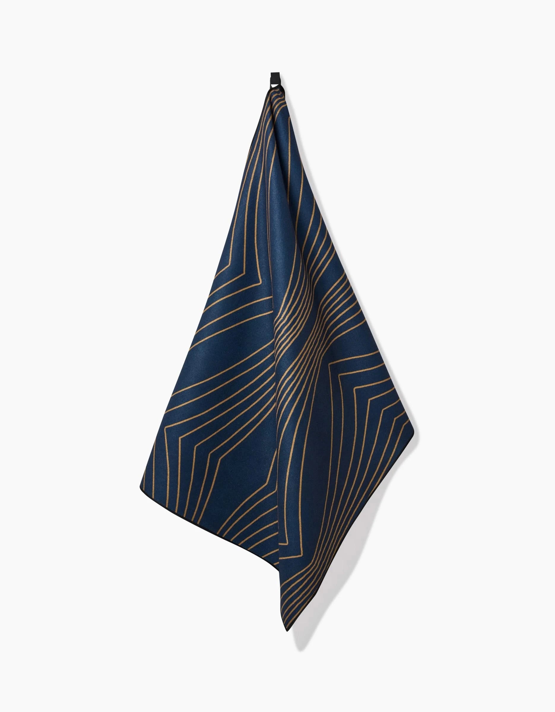 The Amy MacCready Hera towel, a recycled dark blue yoga accessory with an abstract gold geometric line pattern, hangs from a single hook against a plain white background.
