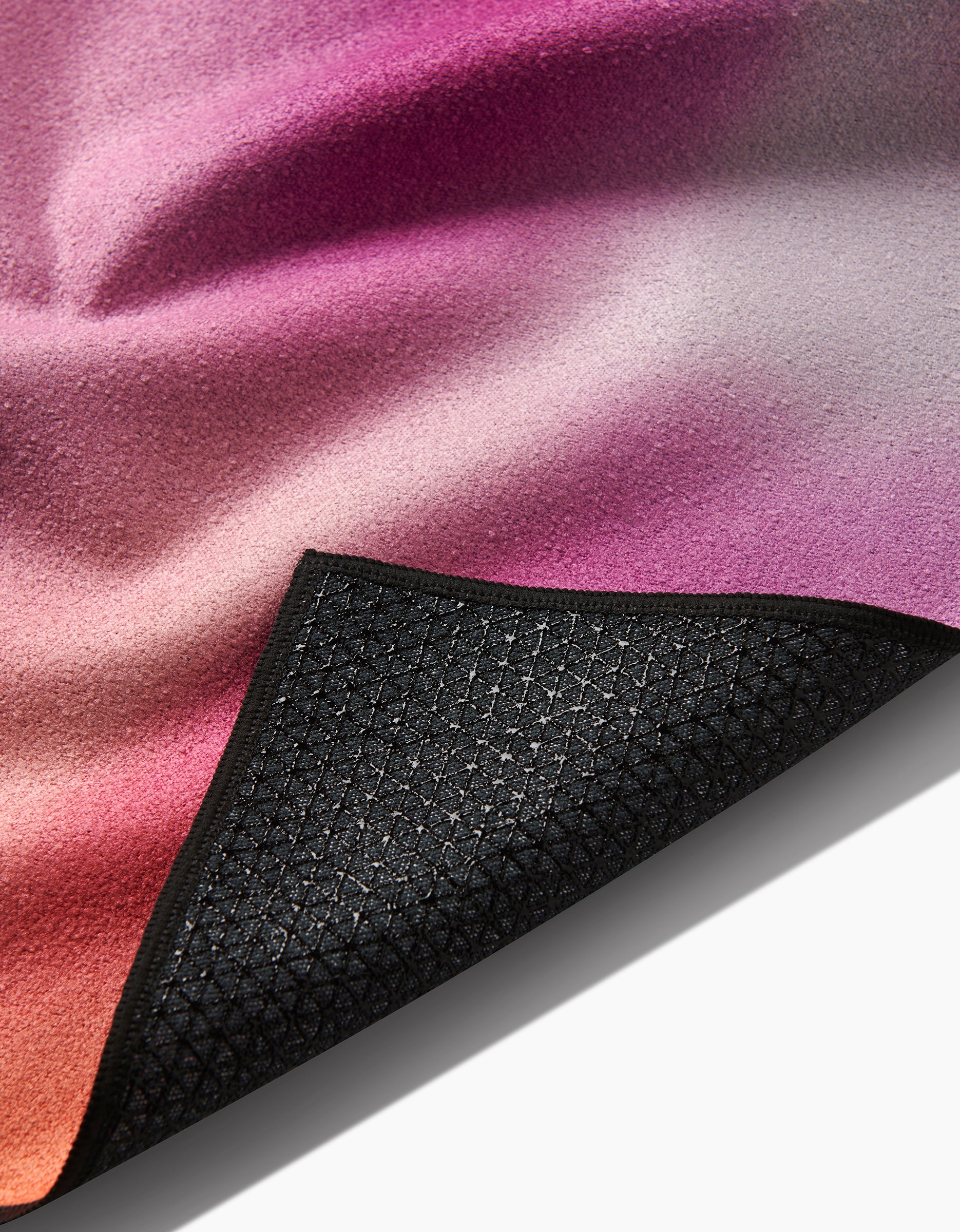 A close-up of the GEOMETRY Magenta yoga towel shows its pink, purple, and orange gradient. A flipped corner reveals the textured black non-slip silicone grip with a grid pattern.